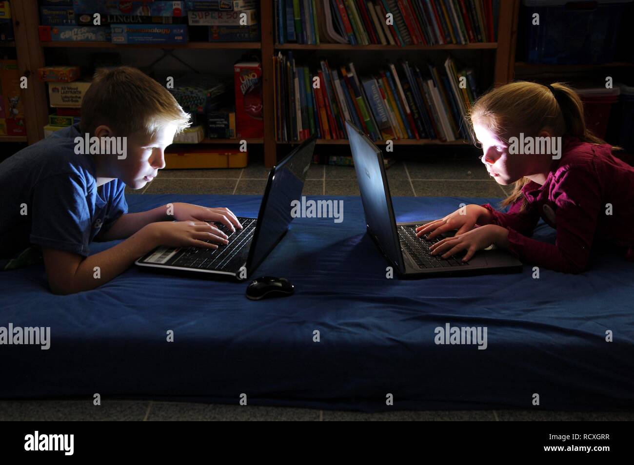 Geschwister, ein Junge, 12 Jahre alt, und ein Mädchen, 10 Jahre alt, Spielen von Computerspielen auf Laptop Computer in Ihrem Zimmer Stockfoto