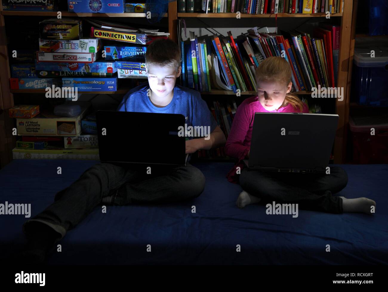 Geschwister, ein Junge, 12 Jahre alt, und ein Mädchen, 10 Jahre alt, Spielen von Computerspielen auf Laptop Computer in Ihrem Zimmer Stockfoto