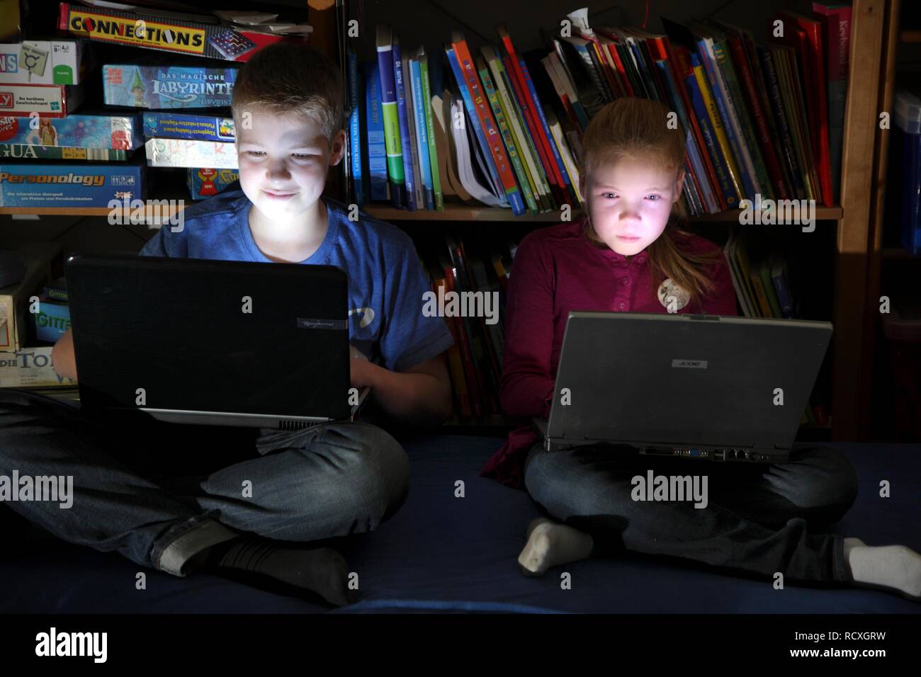 Geschwister, ein Junge, 12 Jahre alt, und ein Mädchen, 10 Jahre alt, Spielen von Computerspielen auf Laptop Computer in Ihrem Zimmer Stockfoto