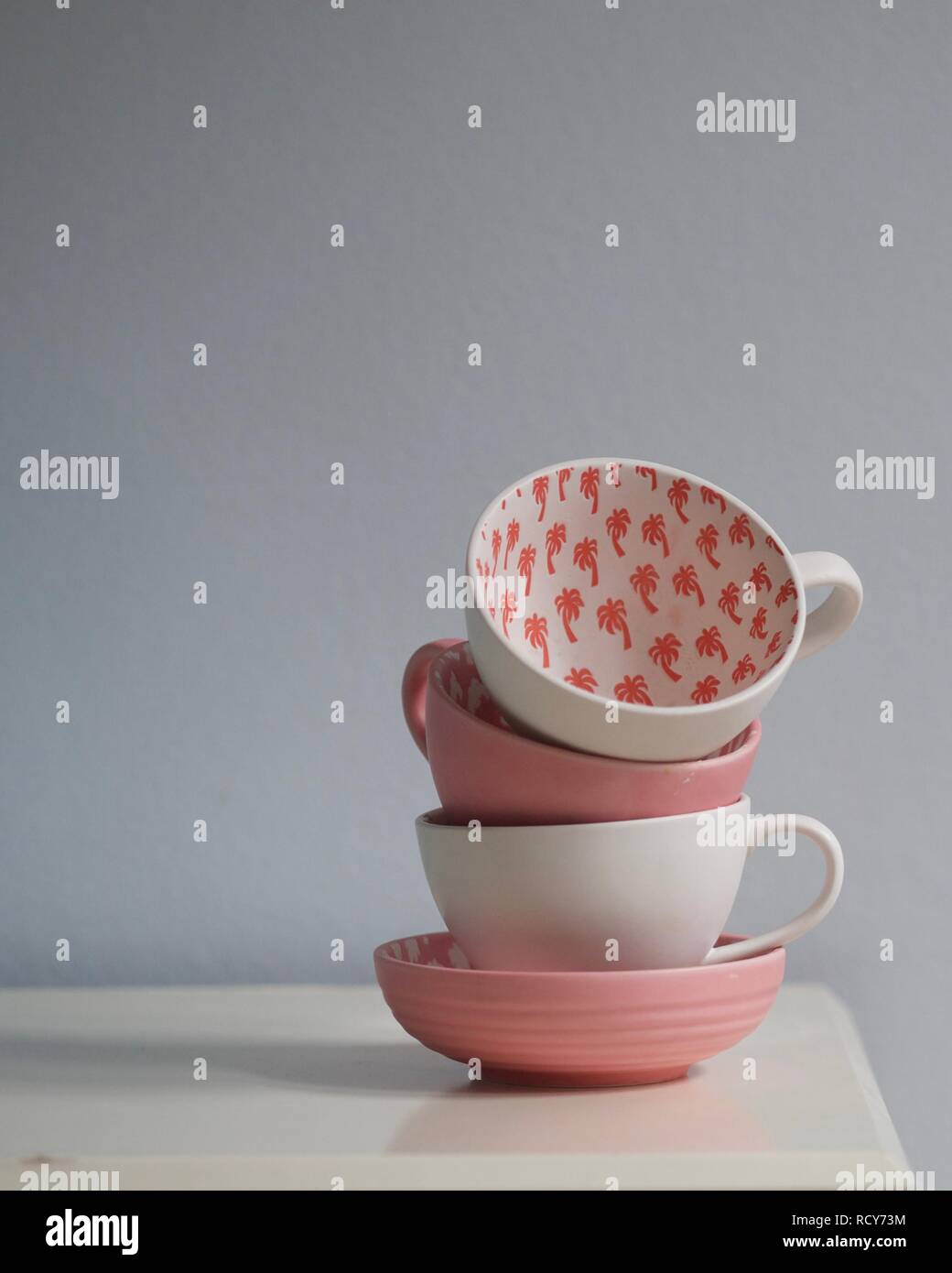 In der Nähe von Coral Pink und White Tea Cups auf weißen Tisch gestapelt. Cups mit Palm Tree Muster eingerichtet. Pantone-Farbe des Jahres 2019 - lebende Koralle. Stockfoto