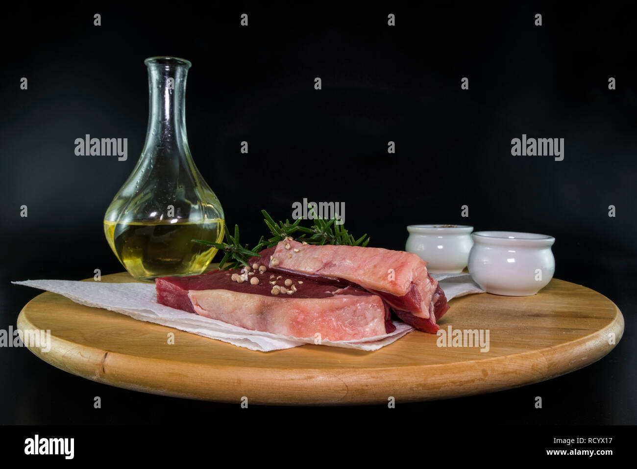 Zwei entrecote Steaks auf einer hölzernen Platte mit Olivenöl Rosmarin Salz und Pfeffer bereit zum Backen Stockfoto