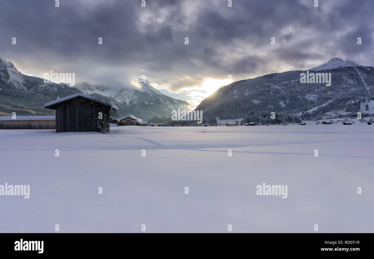 Winter Berge in der Abenddämmerung. Die untergehende Sonne leuchtet, dunkle Wolken. Nebel fällt in das Tal. Stockfoto