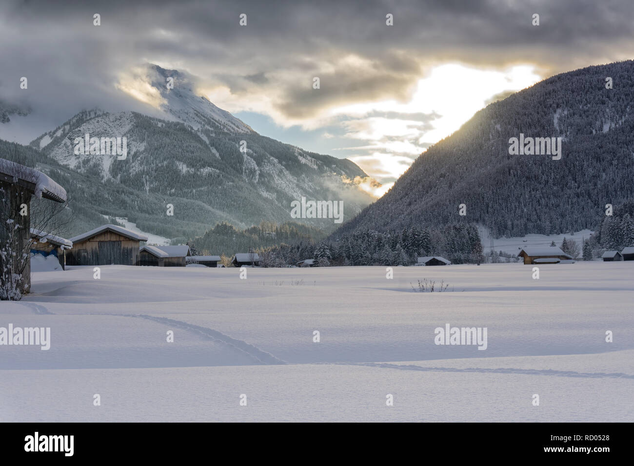 Winter Berge in der Abenddämmerung. Die untergehende Sonne leuchtet, dunkle Wolken. Nebel fällt in das Tal. Stockfoto