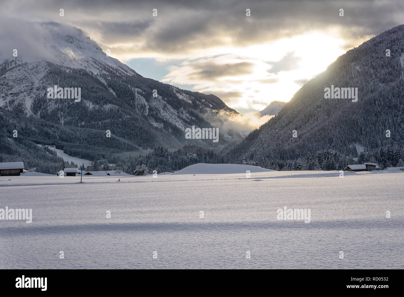 Winter Berge in der Abenddämmerung. Die untergehende Sonne leuchtet, dunkle Wolken. Nebel fällt in das Tal. Stockfoto