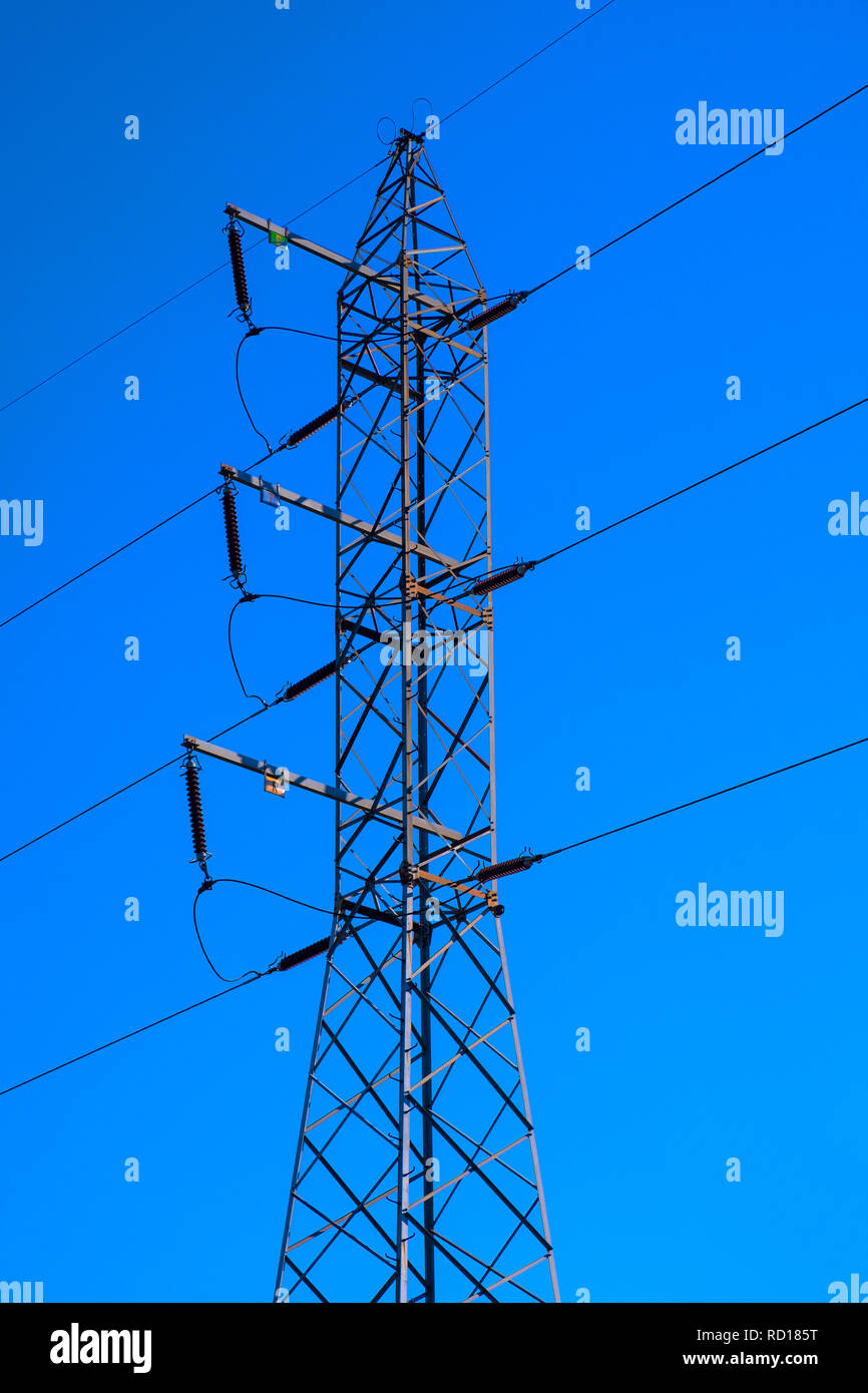 Hochspannungsleitung durch das Metall Bau einer Hochspannung elektrische Pole mit Power Isolatoren und Anschlüsse in einem tiefen Blau unterstützt. Stockfoto
