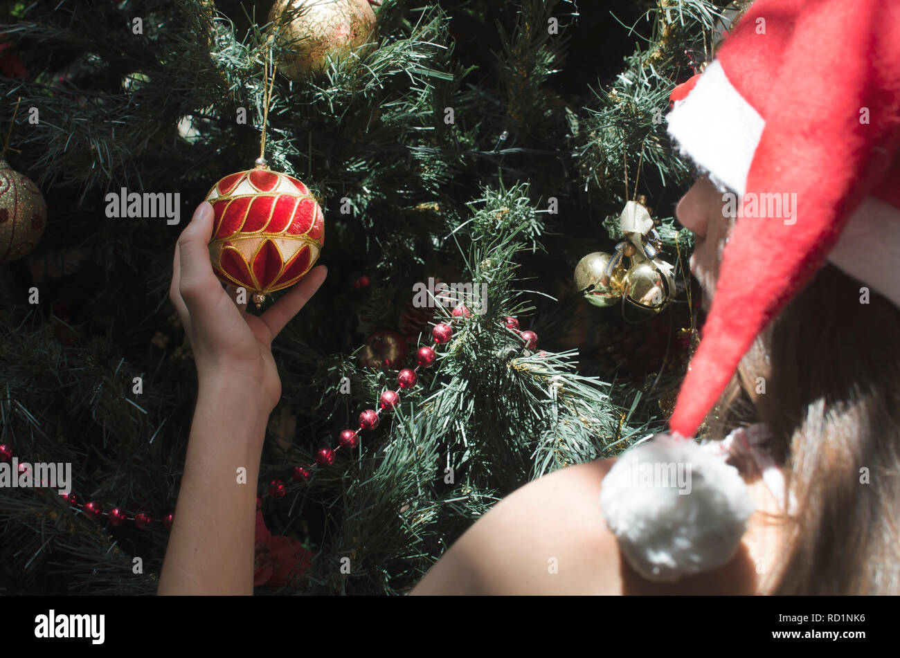 Mädchen mit einem Santa Hat eine Christbaumkugel auf einen Weihnachtsbaum Stockfoto