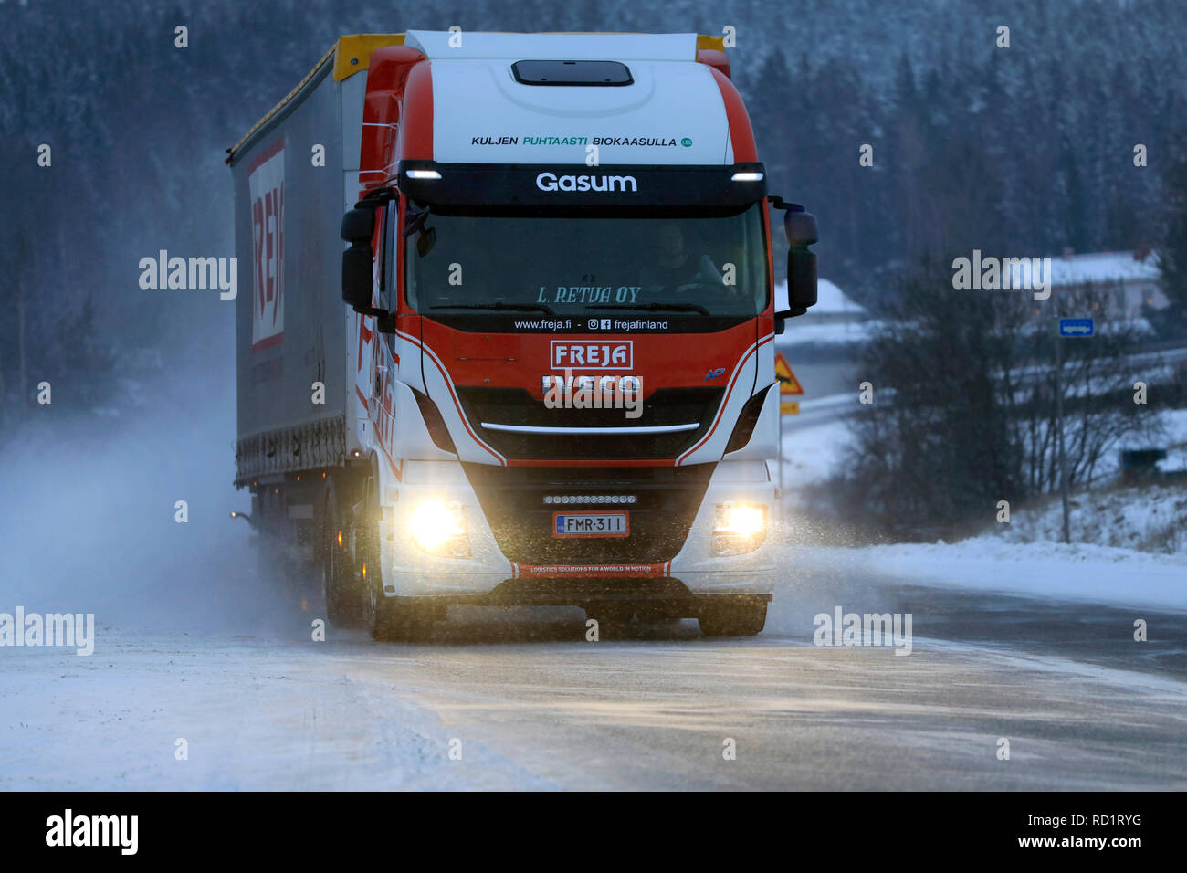 Salo, Finnland - 22. Dezember 2018: Biogas betrieben Iveco Stralis NP LKW L. Retva Oy zieht FREJA Trailer zusammen verschneite Autobahn auf einem blauen winter Abend. Stockfoto