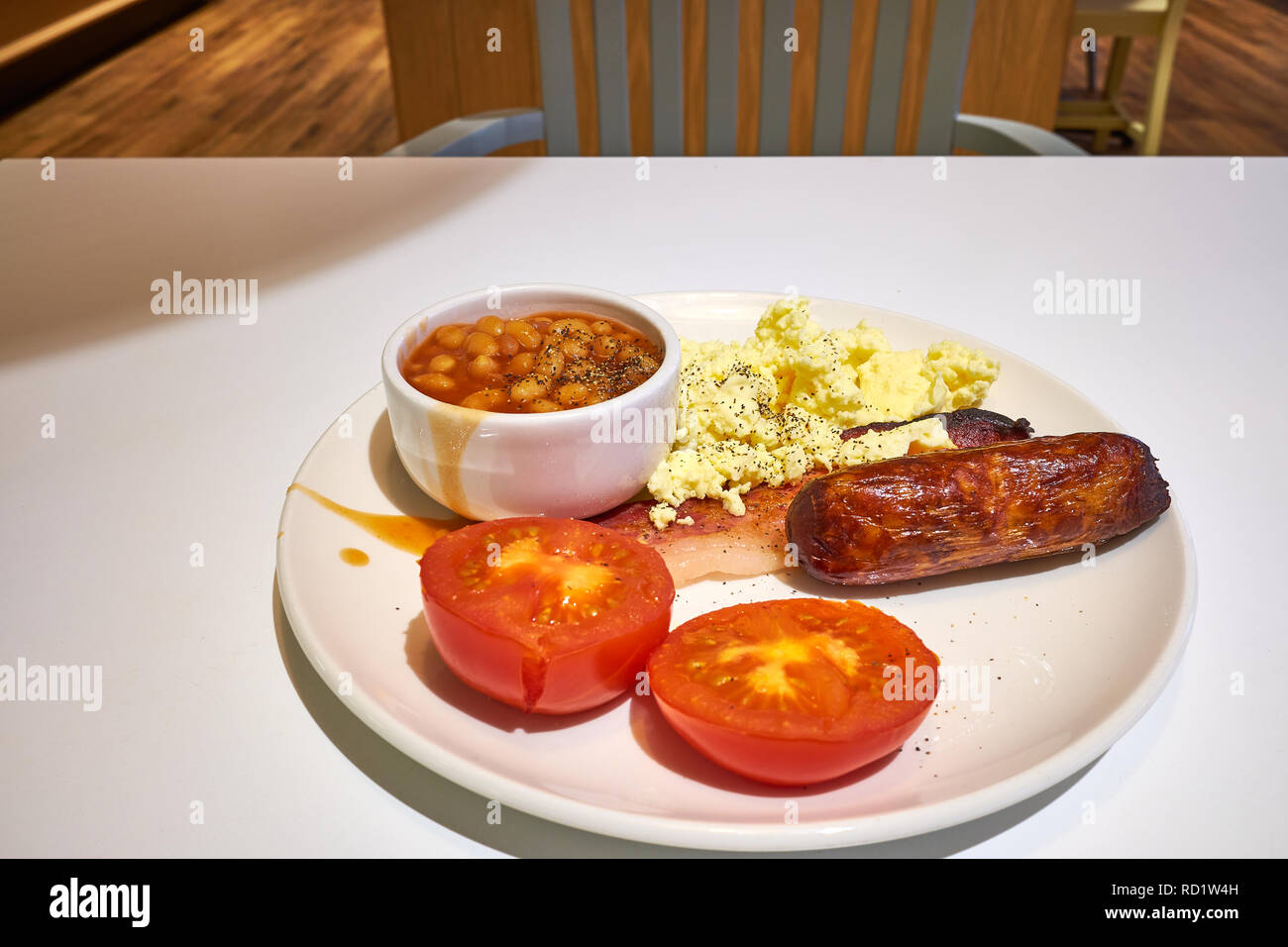 Englisches Frühstück mit Wurst, Speck, gegrillte Tomaten, Rührei und gebackene Bohnen auf einem Tisch in einem Café. Stockfoto