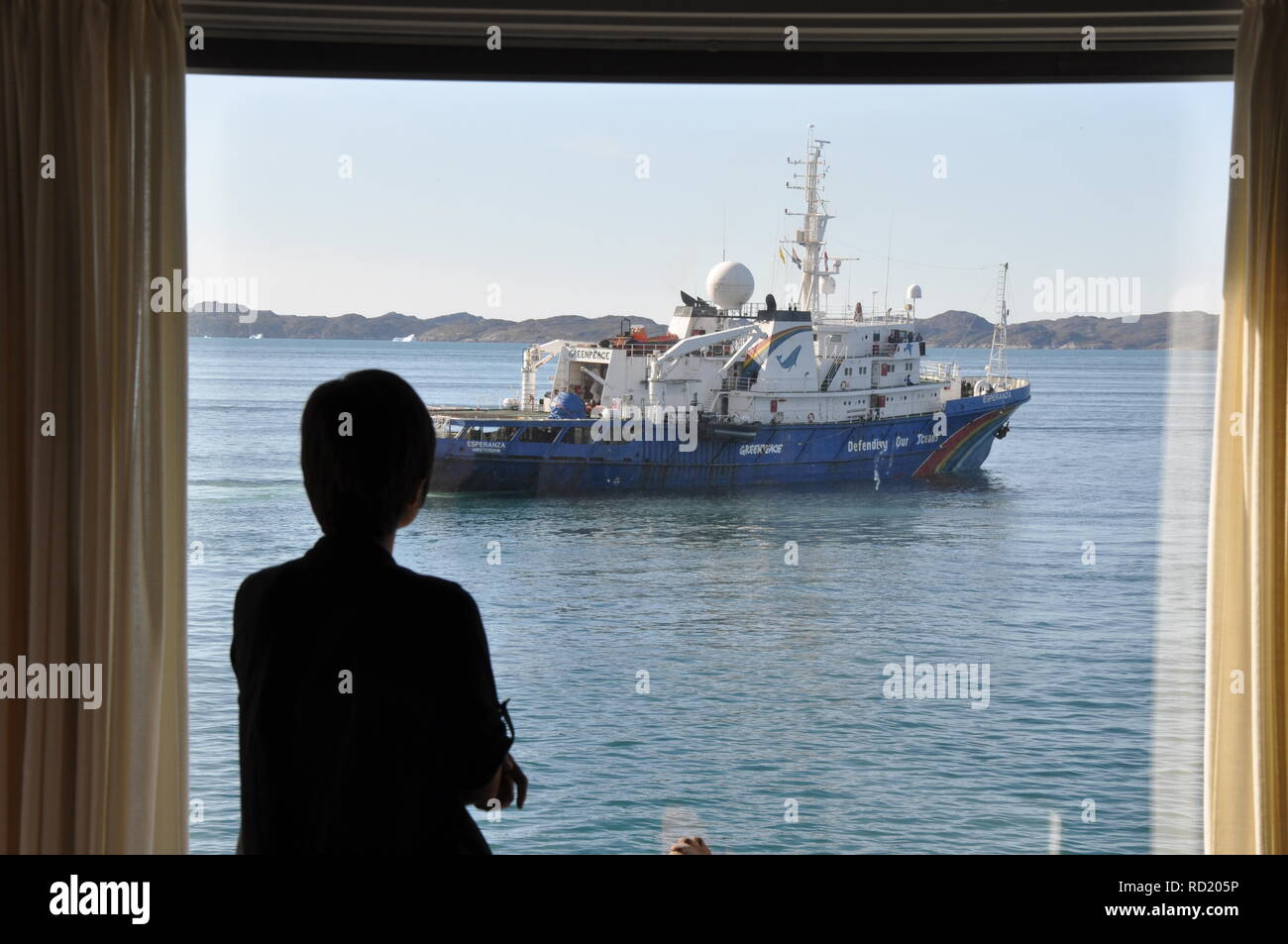 Eine Frau schauen aus dem Fenster Ihres Hauses auf dem Greenpeace Schiff in der grönländischen Hauptstadt Nuuk Stockfoto