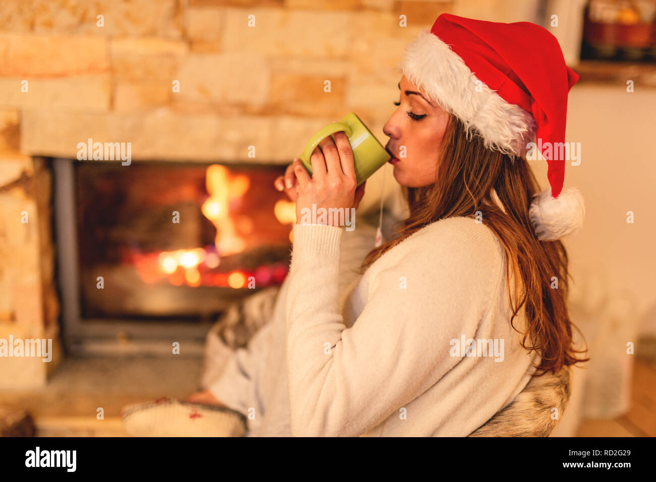 Schöne junge lächelnde Frau genießen eine Tasse Tee vor dem Kamin in Weihnachten Abend. Stockfoto