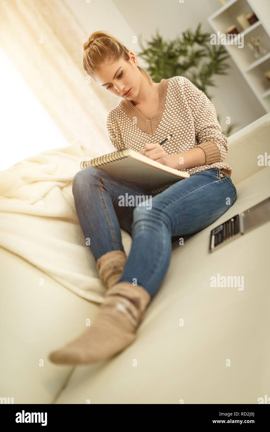 Schöne junge lächelnde Frau entspannend durch die Zeichnung in ein Skizzenbuch mit Buntstiften zu Hause. Stockfoto