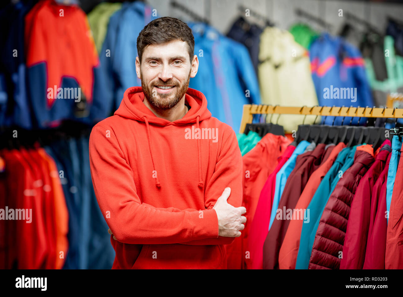 Porträt von einem stattlichen Mann, der als Verkäufer oder Kunde in der Kleidung Abteilung mit Jacken in einem Sportgeschäft Stockfoto