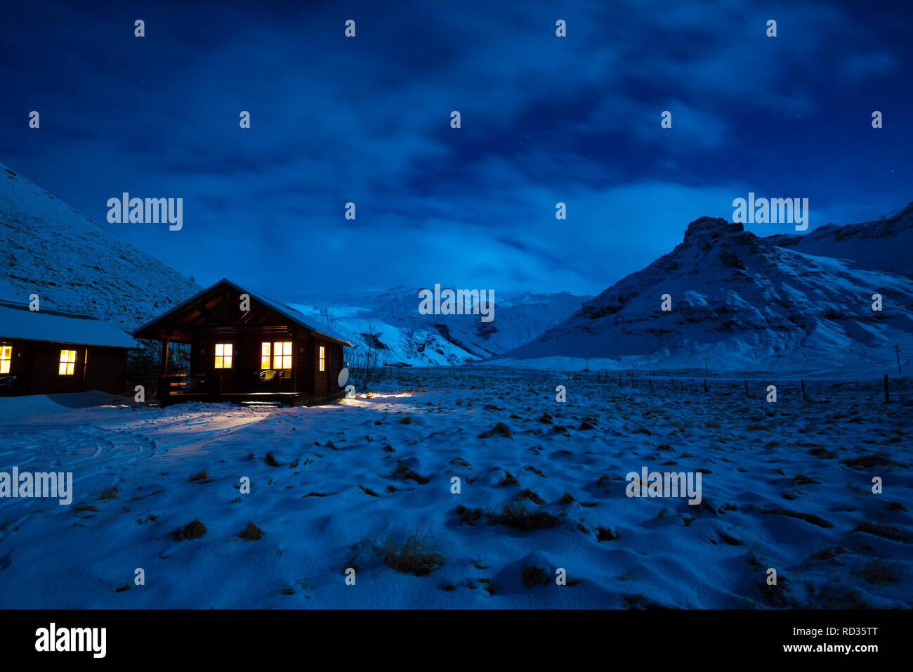 Winter Bild von ein Holzhaus mit Licht vom Fenster. Landschaft mit Mondlicht auf dem Schnee mit Bergen im Hintergrund. South Island. Stockfoto