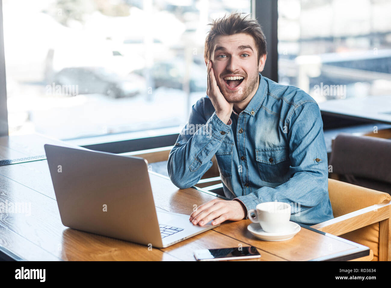 Oh mein Gott!!! Portrait von Happy toothy Lächeln bärtige junge Freiberufler in Blue Jeans shirt sind allein sitzt im Cafe und in neuen Vorschlag für eine Arbeit Stockfoto