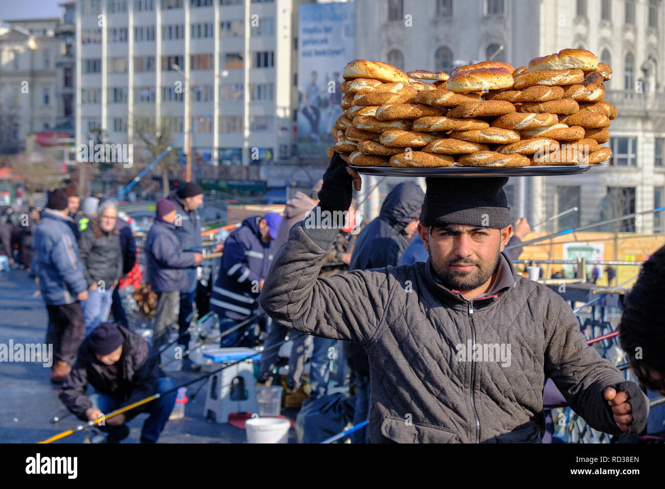 Istanbul, Türkei: Mann verkauf von simit (runde Traditionelles türkisches Brot) an die Fischer auf der Galata Brücke. Portrait mit dem Verkäufer mit simit auf dem Kopf Stockfoto