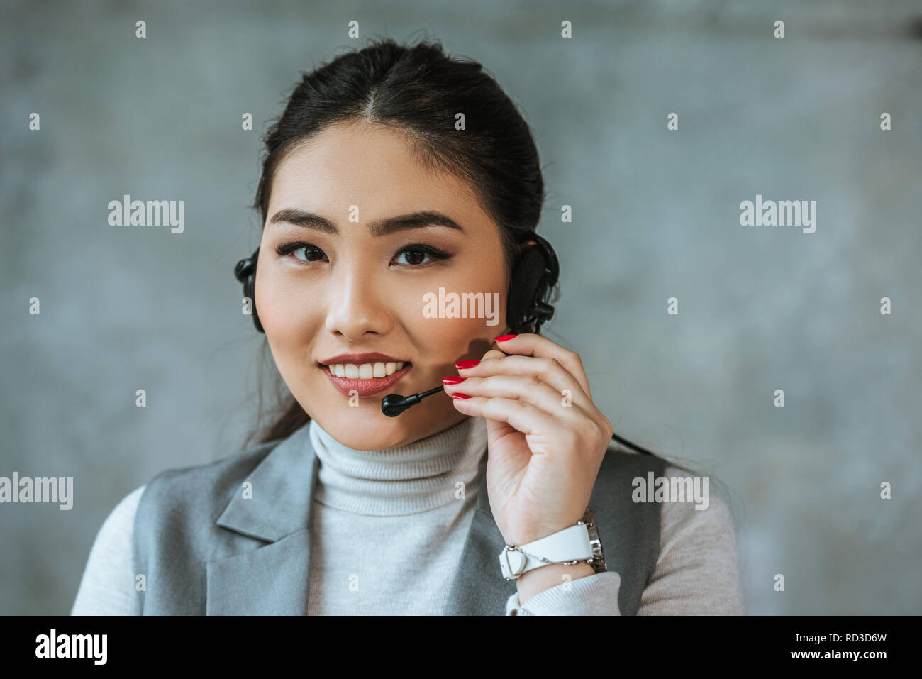 Schöne junge asiatische Call Center Betreiber lächelnd an Kamera auf Grau Stockfoto