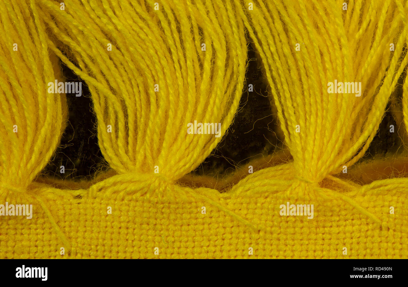 Overhead Detailansicht von Garn Quasten an den Rand eines gelben Tischset. Es ist ein sich wiederholendes Muster der Quasten. Stockfoto