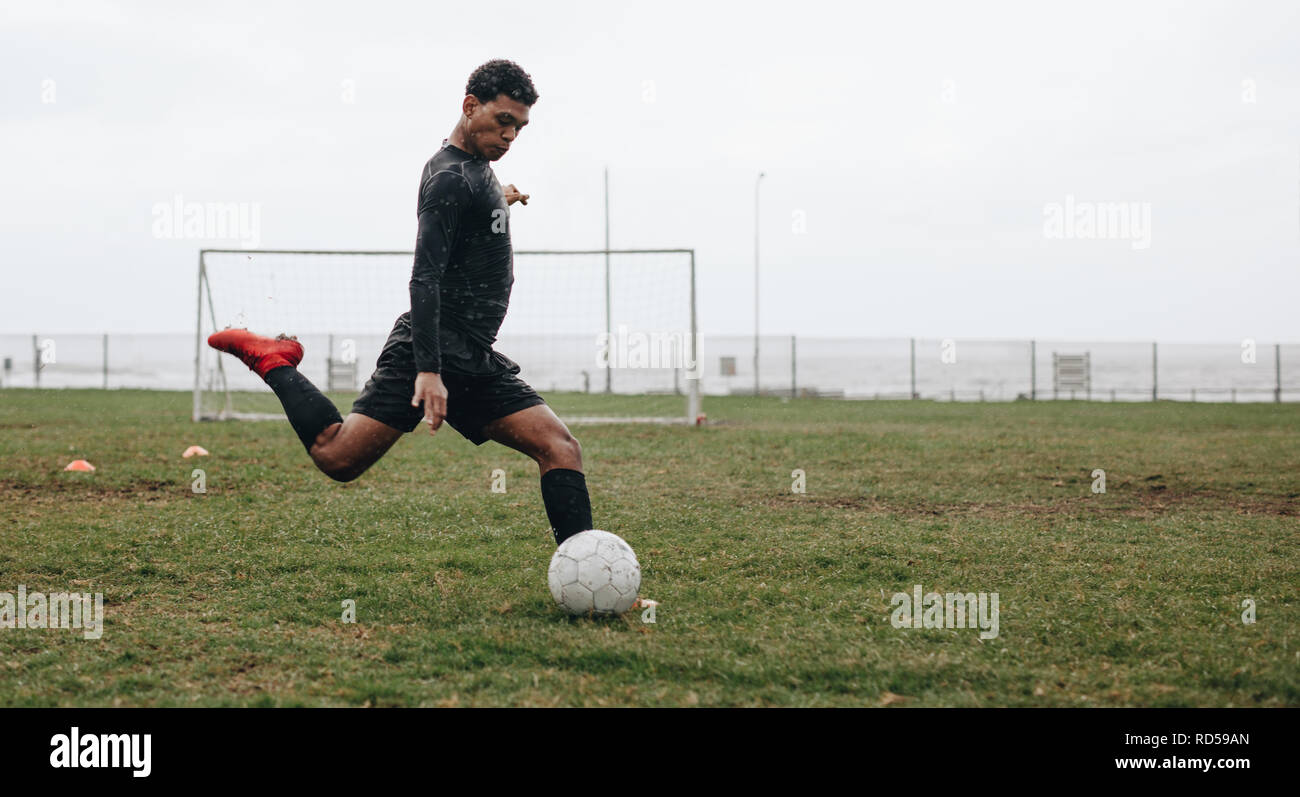 Fußballspieler auf dem Feld, der gerade den Ball kickt. Mann spielt Fußball auf dem Feld an einem bewölkten Morgen. Stockfoto