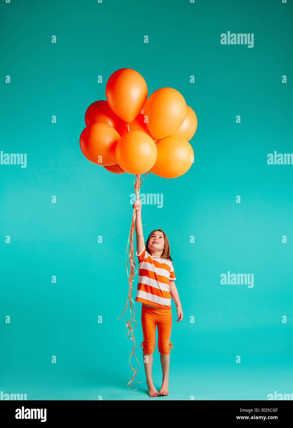 Cute girl Holding orange Luftballons auf blauem Hintergrund. Die ganze Länge der Mädchen mit Bündel von Helium Luftballons. Stockfoto