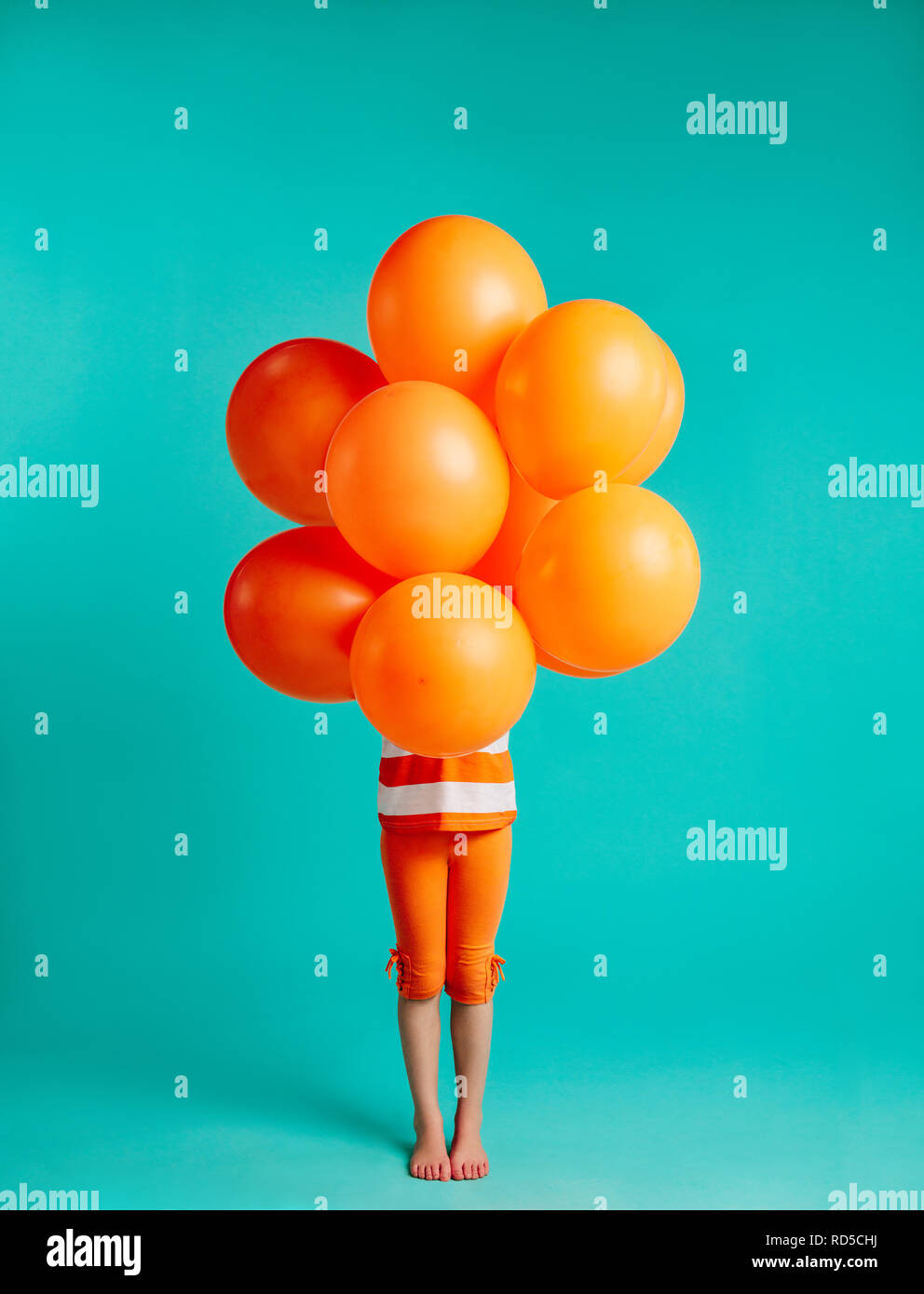 Girl Holding orange Luftballons vor auf blauem Hintergrund. Volle Länge des kleinen Mädchen mit Bündel von Helium Luftballons. Stockfoto