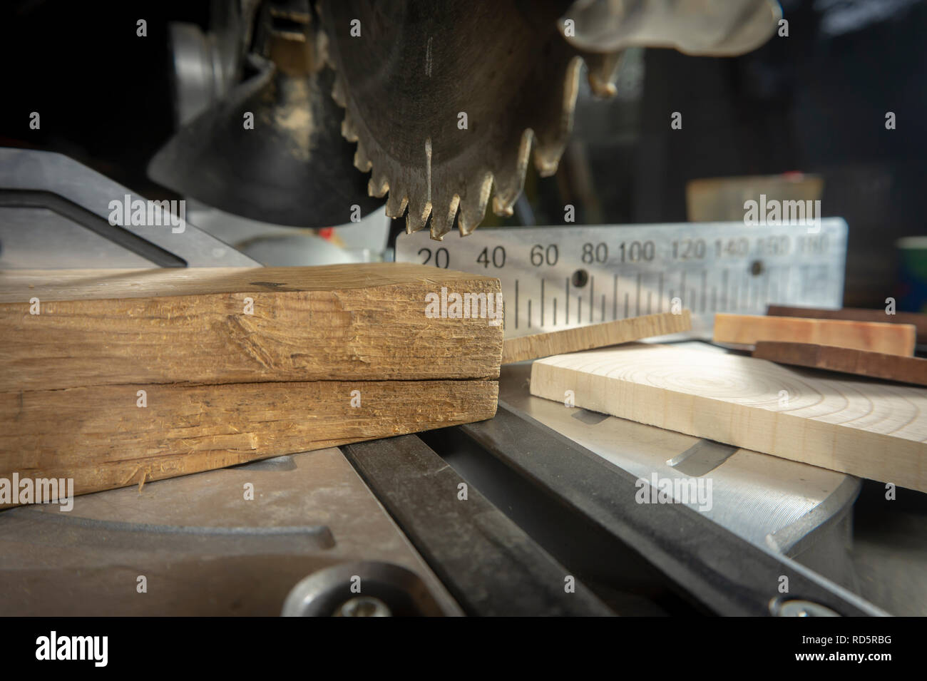 Zähne auf einer kreisförmigen Motorsäge in Nahaufnahme mit verschiedenen Bausteinen aus Holz und Metall Maßstab für Schnittlängen in einem Holzbearbeitung workshop Stockfoto
