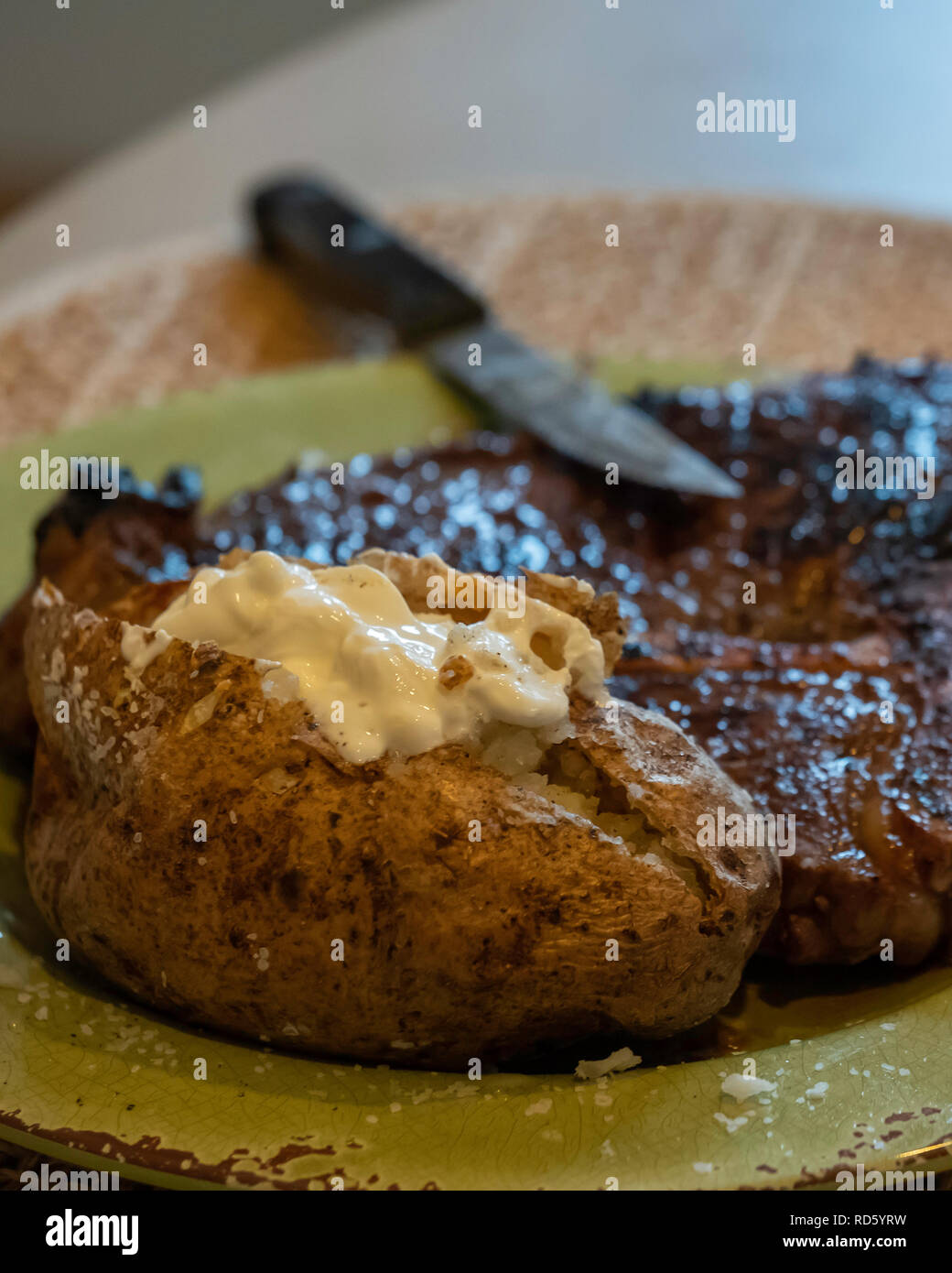 Eine gebratene Ribeye, oder Rib Eye Steak gekocht Medium gut mit einer gebackenen Kartoffel und saure Sahne auf einem Teller zu tun. USA. Stockfoto