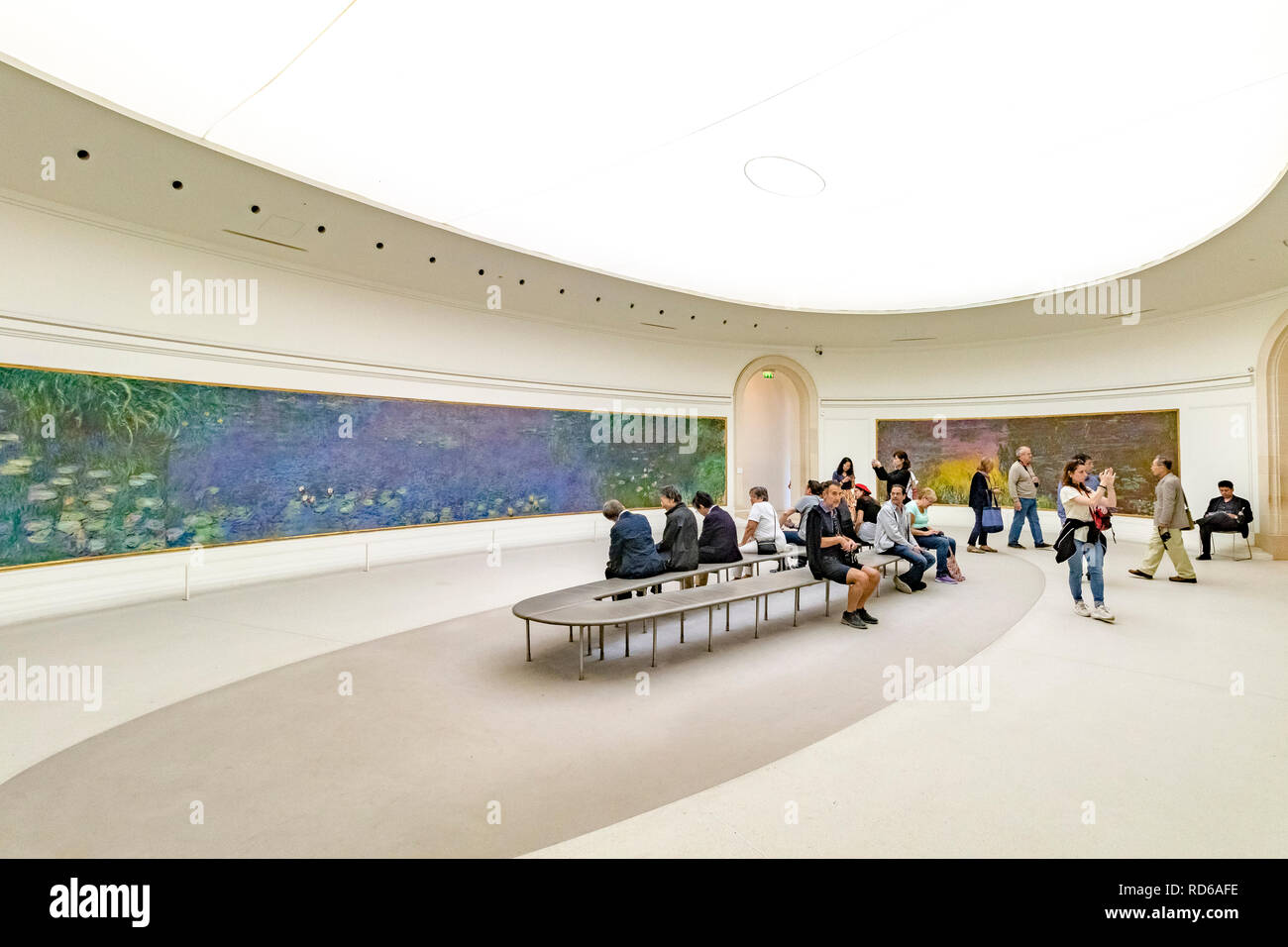 Menschen, die die Seerosen von Claude Monet in geschwungenen Tafeln in einem ovalen Raum in der Orangerie oder im Musée de l'Orangerie in Paris, Frankreich, betrachten Stockfoto