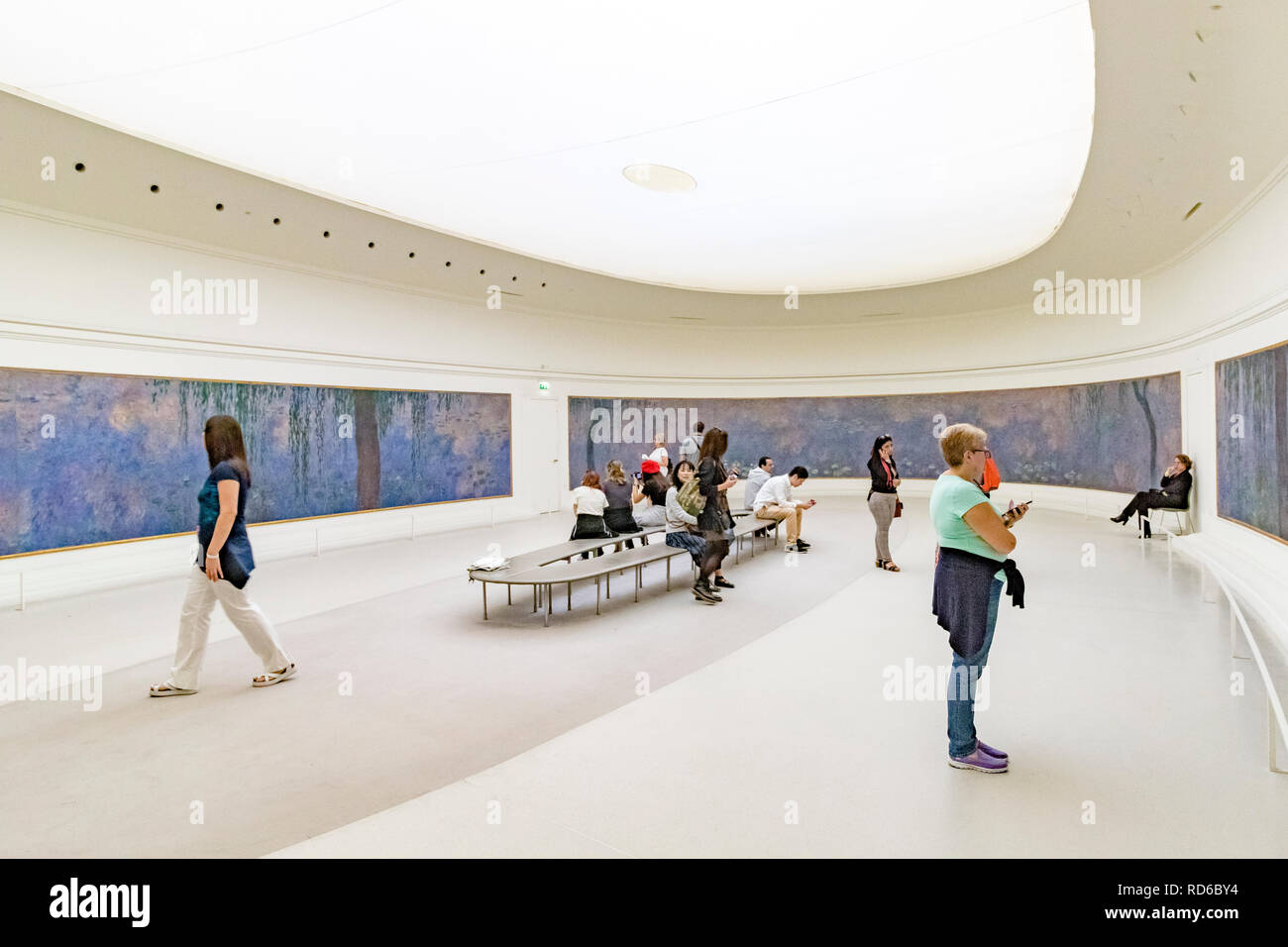 Menschen, die die Seerosen von Claude Monet in geschwungenen Tafeln in einem ovalen Raum in der Orangerie oder im Musée de l'Orangerie in Paris, Frankreich, betrachten Stockfoto