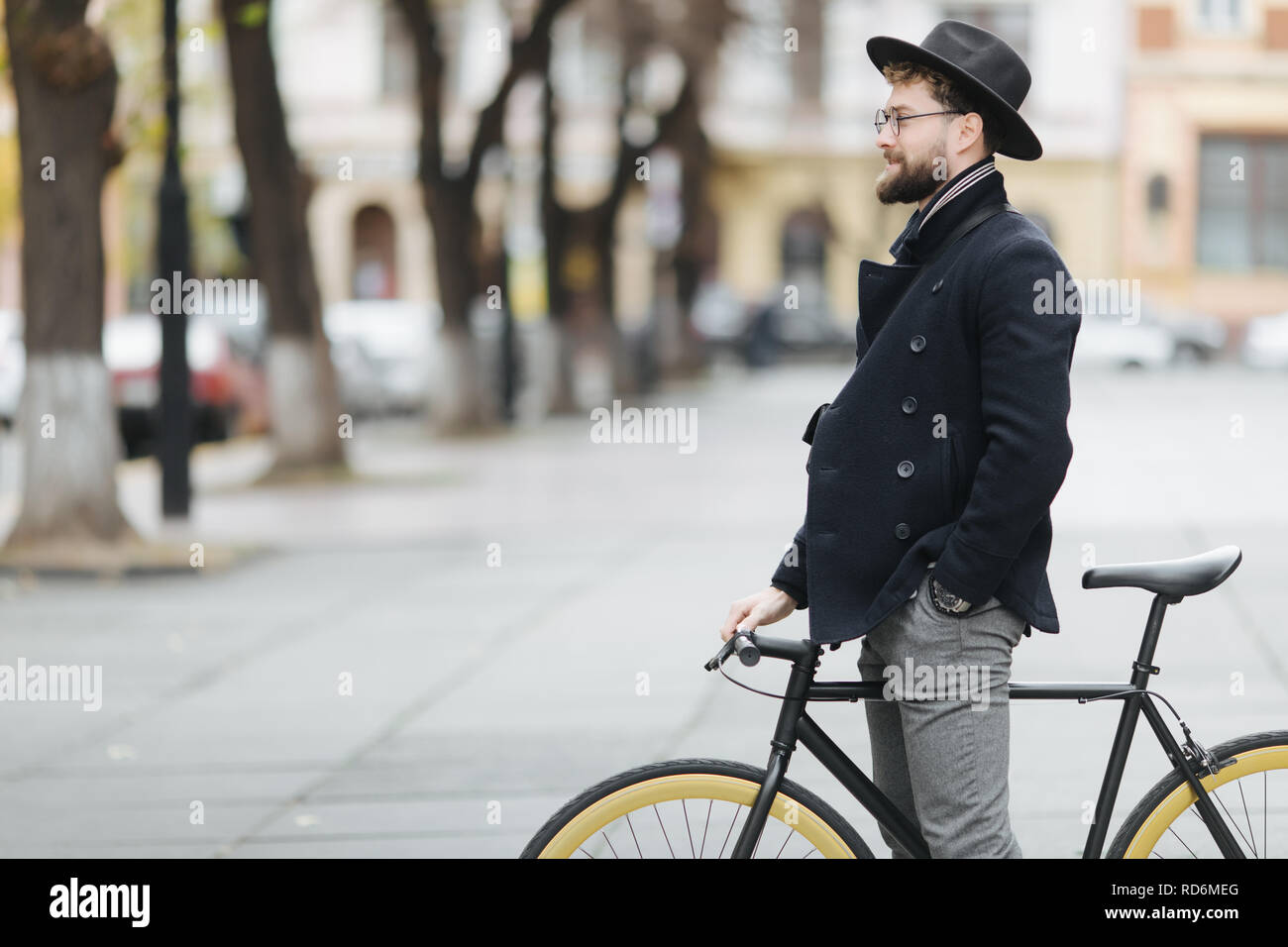 Gut aussehender bärtiger Mann in Gläsern und Kappe mit Fahrrad und lächelnd Stockfoto