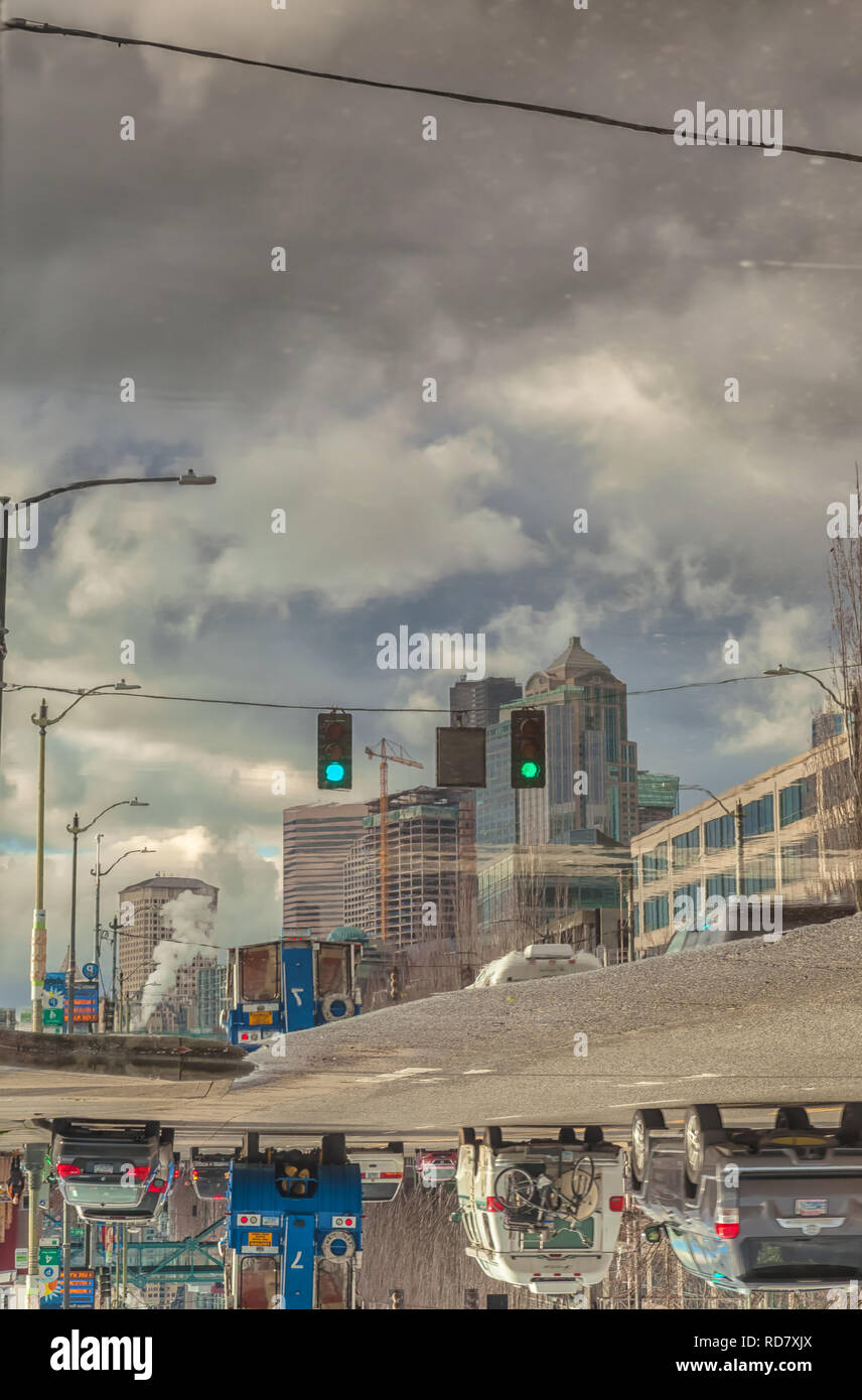 Reflexionen von Seattle Waterfront City Gebäude auf einem großen Regenwasser Pfütze nach einem Wintersturm, der in der Innenstadt von Seattle, Washington, United States. Stockfoto