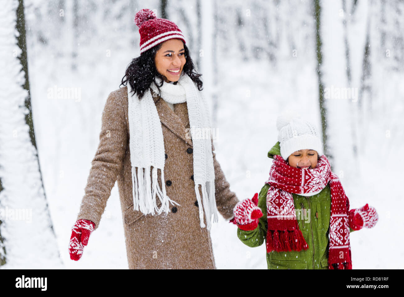Fröhlich afrikanische amerikanische Mamma und niedlichen Kind stehen bei Schneefall im Winter Park Stockfoto