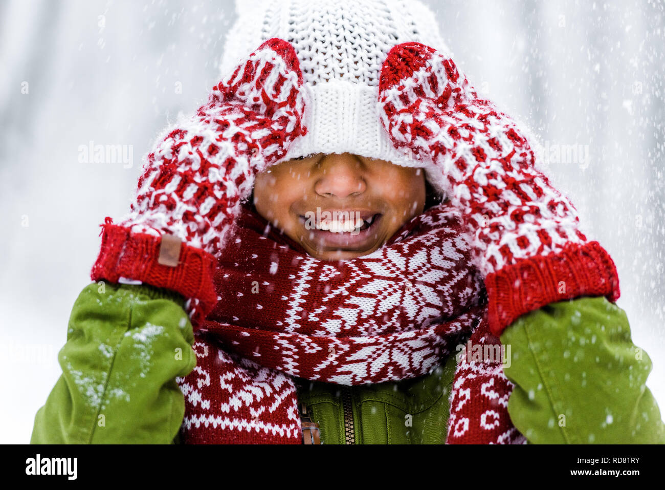 Cute afrikanische amerikanische Kind mit Strickmütze zog über Augen lächeln bei Schneefall Stockfoto