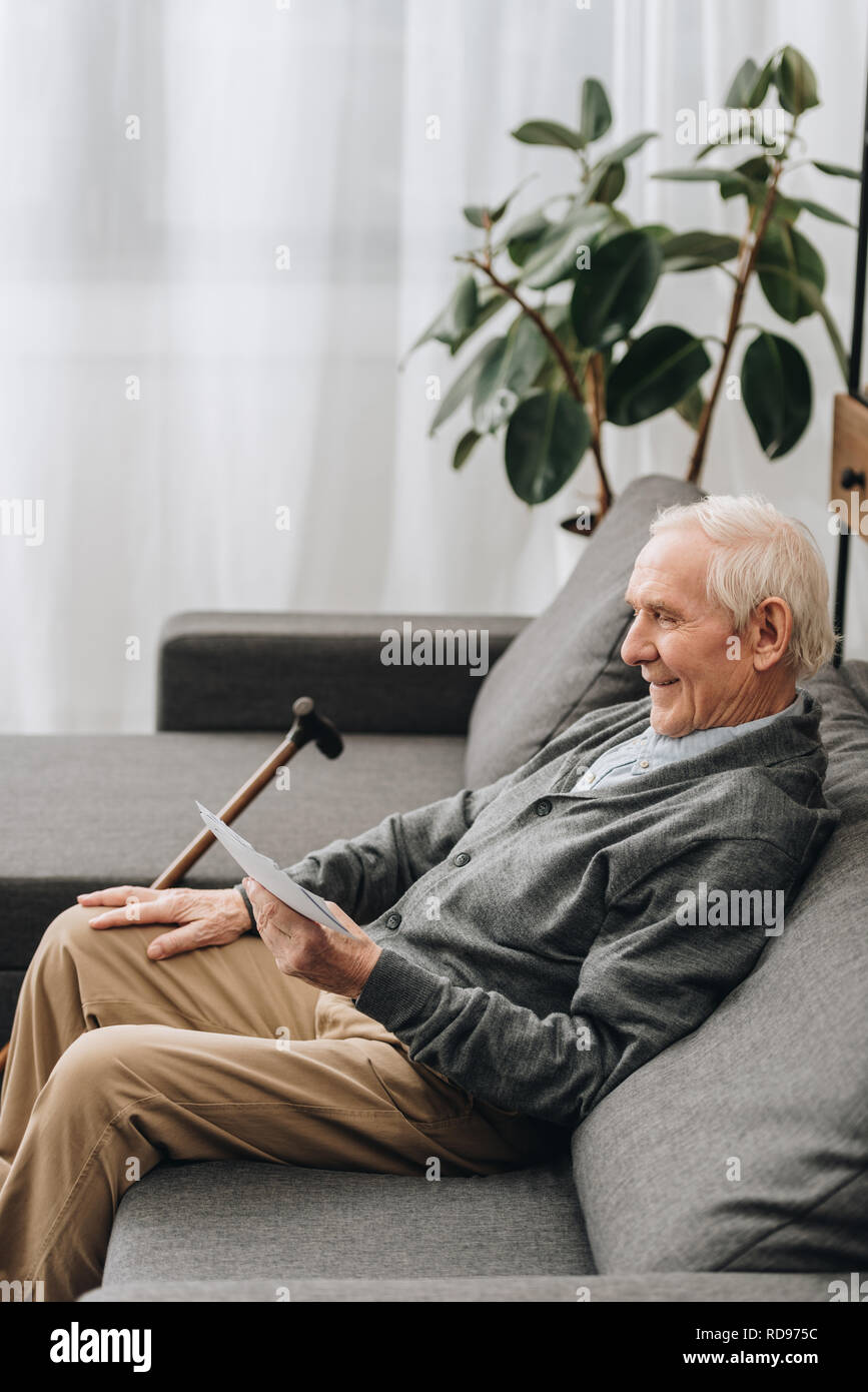 Lächelnd Rentner mit grauem Haar das Betrachten von Fotos und das Sitzen auf dem Sofa Stockfoto
