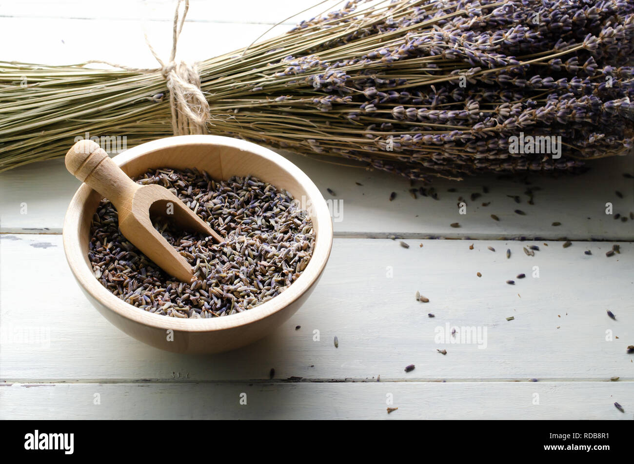 Schüssel von getrockneten Kräuter lavendel Blütenknospen mit Holz- Schaufel auf weiß lackiertes Holz plank Tabelle. Bindfaden Haufen Stämme hinter sich. Stockfoto