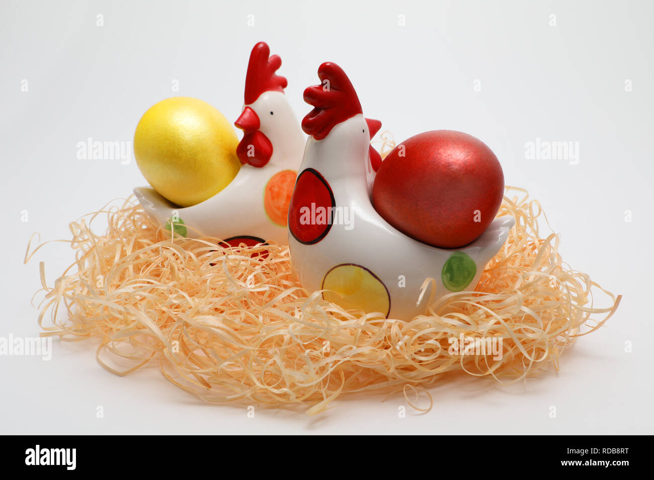 Zwei bunte Ostereier Farben rot und gold in zwei toy Legehennen in einem Nest auf weißem Hintergrund, Feder Bild. Ostern Konzept. Stockfoto