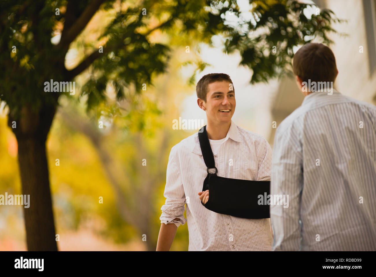 Junge mit Arm in der Schlinge im Gespräch mit Freund Stockfoto