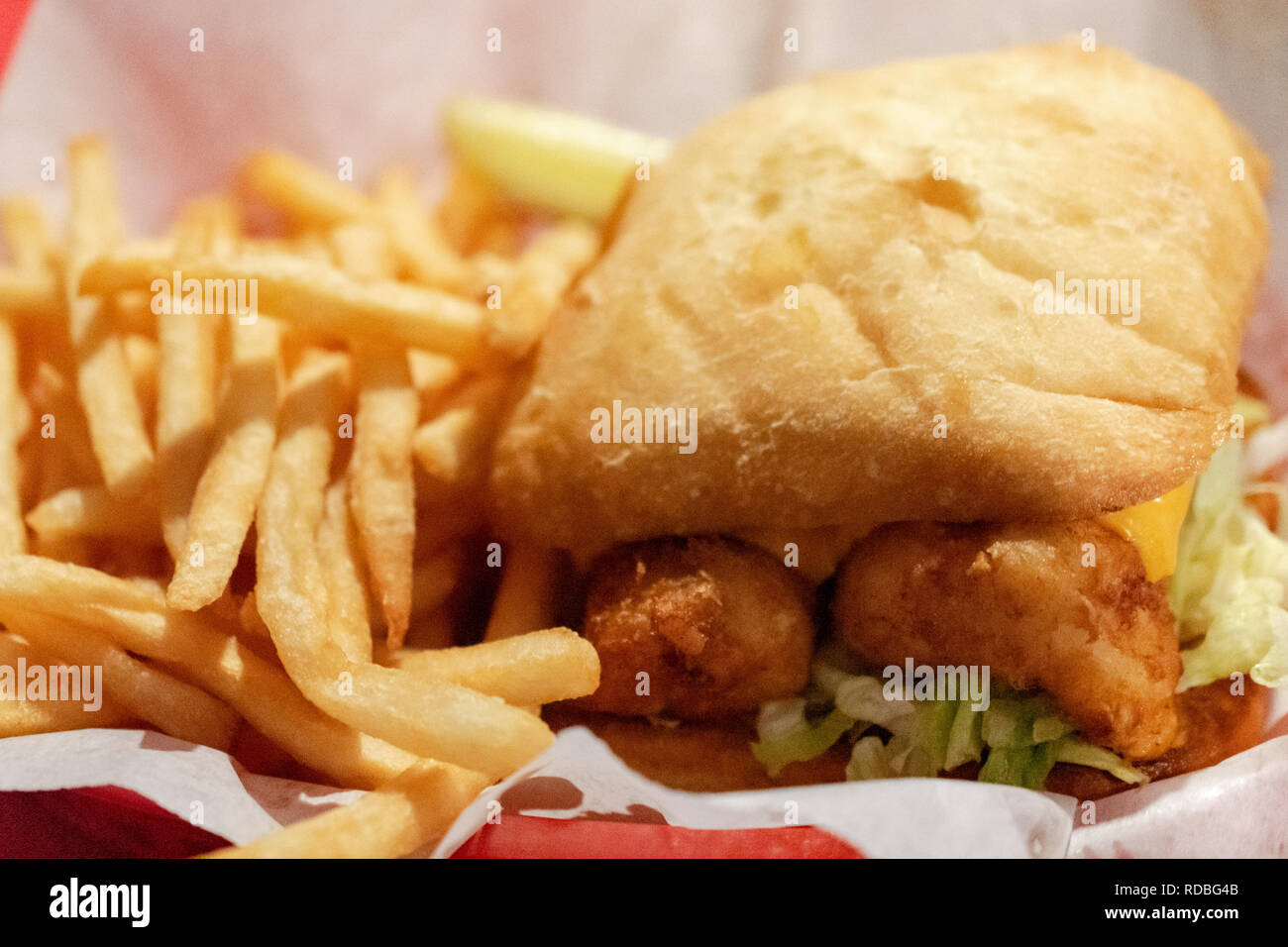 Nahaufnahme der frittierten Fisch Sandwich in einem roten Korb mit Papierstreifen. Pommes frites entlang Seite Sandwich. Pickle im Hintergrund. Stockfoto