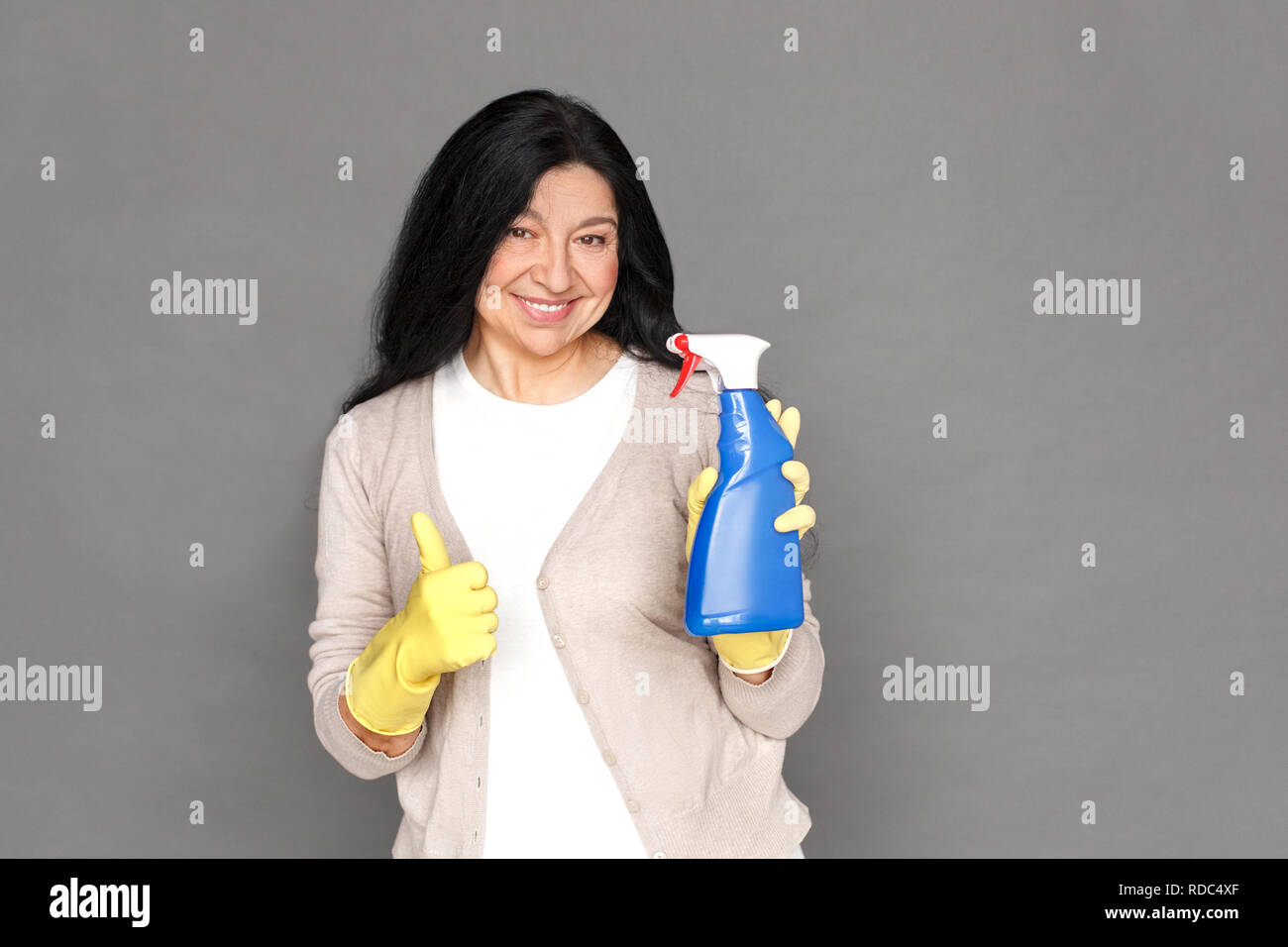 Freestyle. Reife lady in Gummihandschuhe isoliert auf Grau mit Spray Daumen hoch, lächeln, glücklich Stockfoto