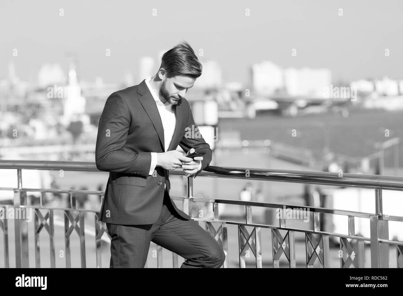 Geschäftsmann mit Smartphone auf der Terrasse am Stadtbild, Business Kommunikation. Mann in Anzug mit Handy, neue Technologie. Business Kommunikation, neue Technologien, sms. Das moderne Leben, Lifestyle Stockfoto