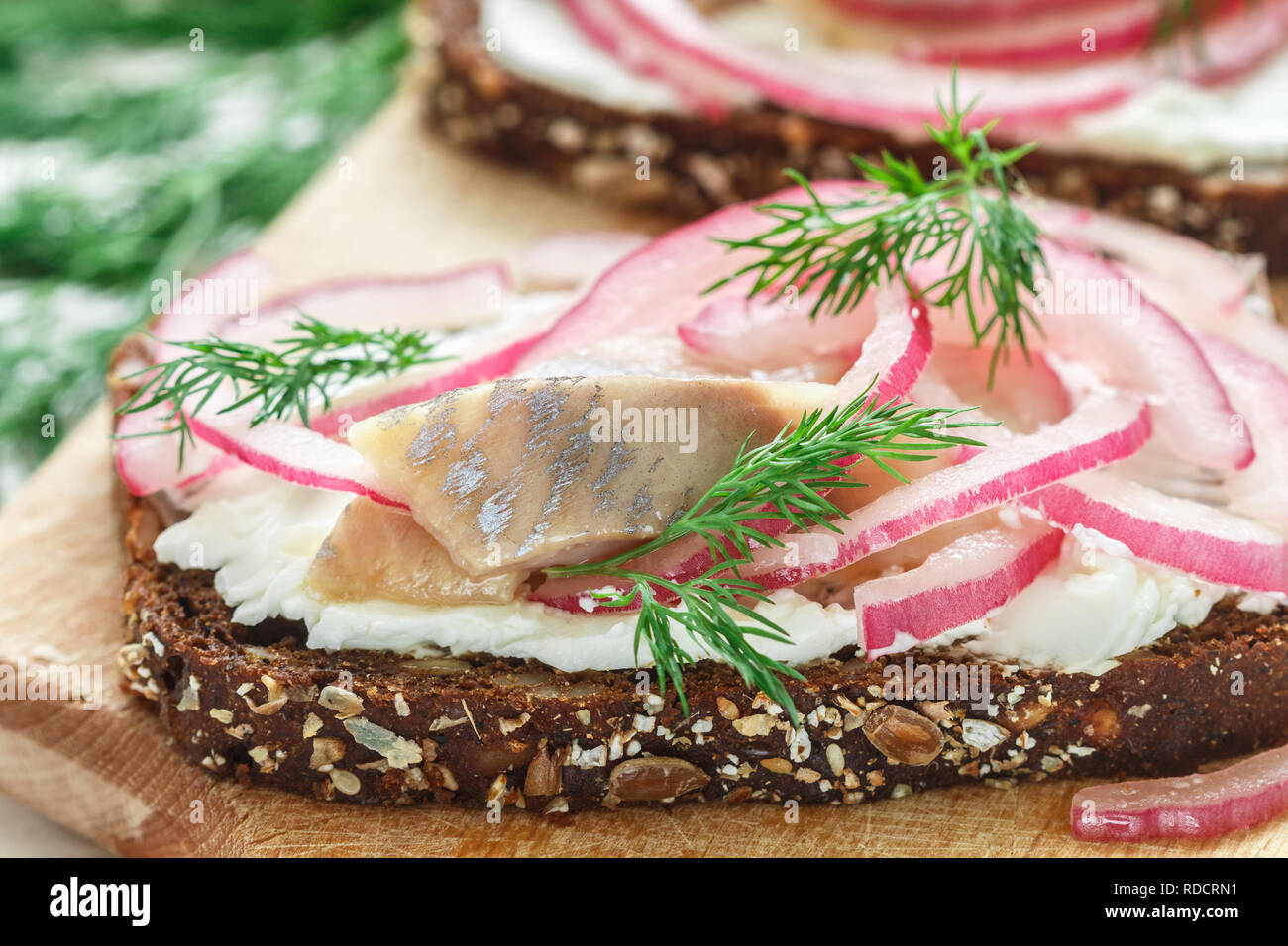 Sandwich mit gesalzenem Fisch (Hering, Makrele), Hüttenkäse (Ricotta), Dill und eingelegte rote Zwiebeln auf Roggenbrot mit Samen zu öffnen. Gourmet Snack. Sele Stockfoto
