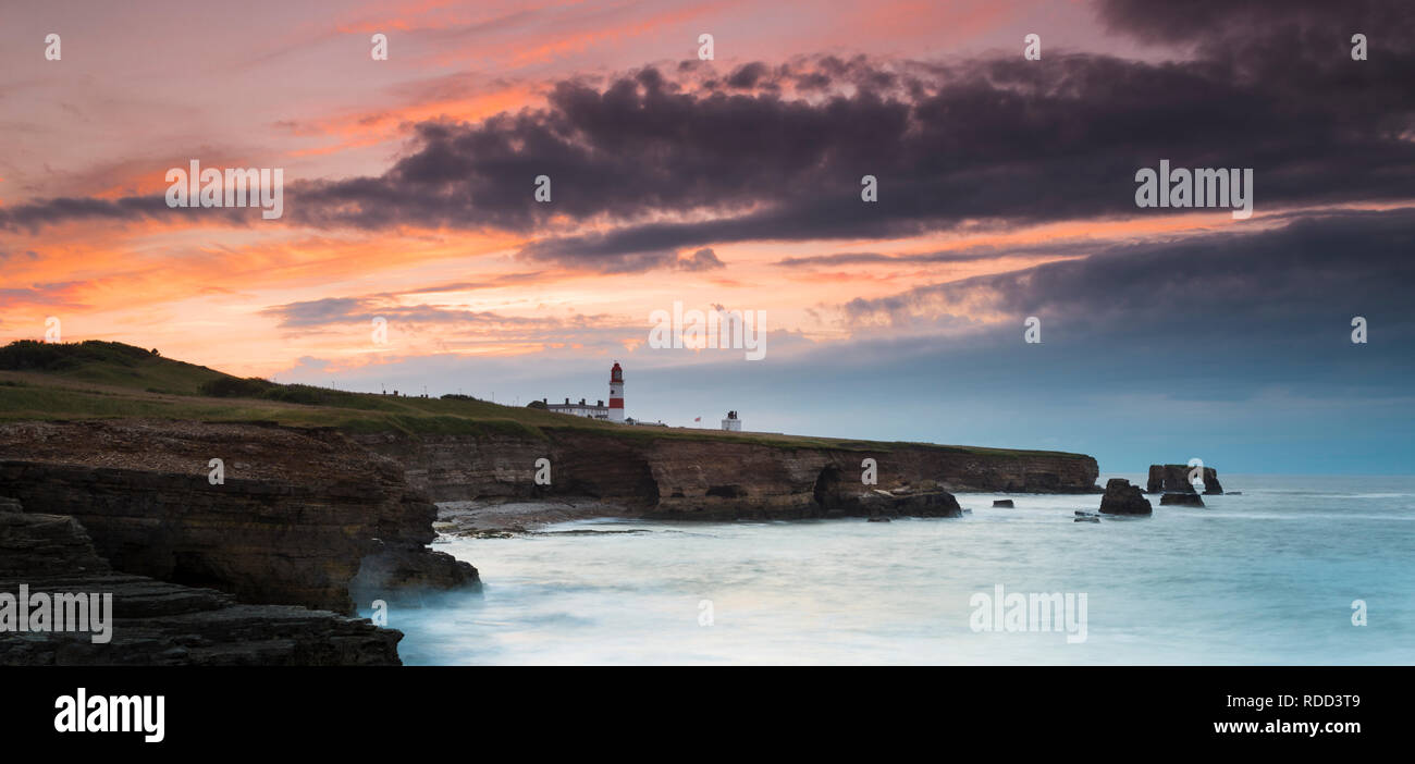 Dramatische Wolken Rückzug als Sonnenuntergang leuchtet der Himmel über Souter Leuchtturm, während das Meer stürzt gegen die Klippen an der nordöstlichen Küste Stockfoto