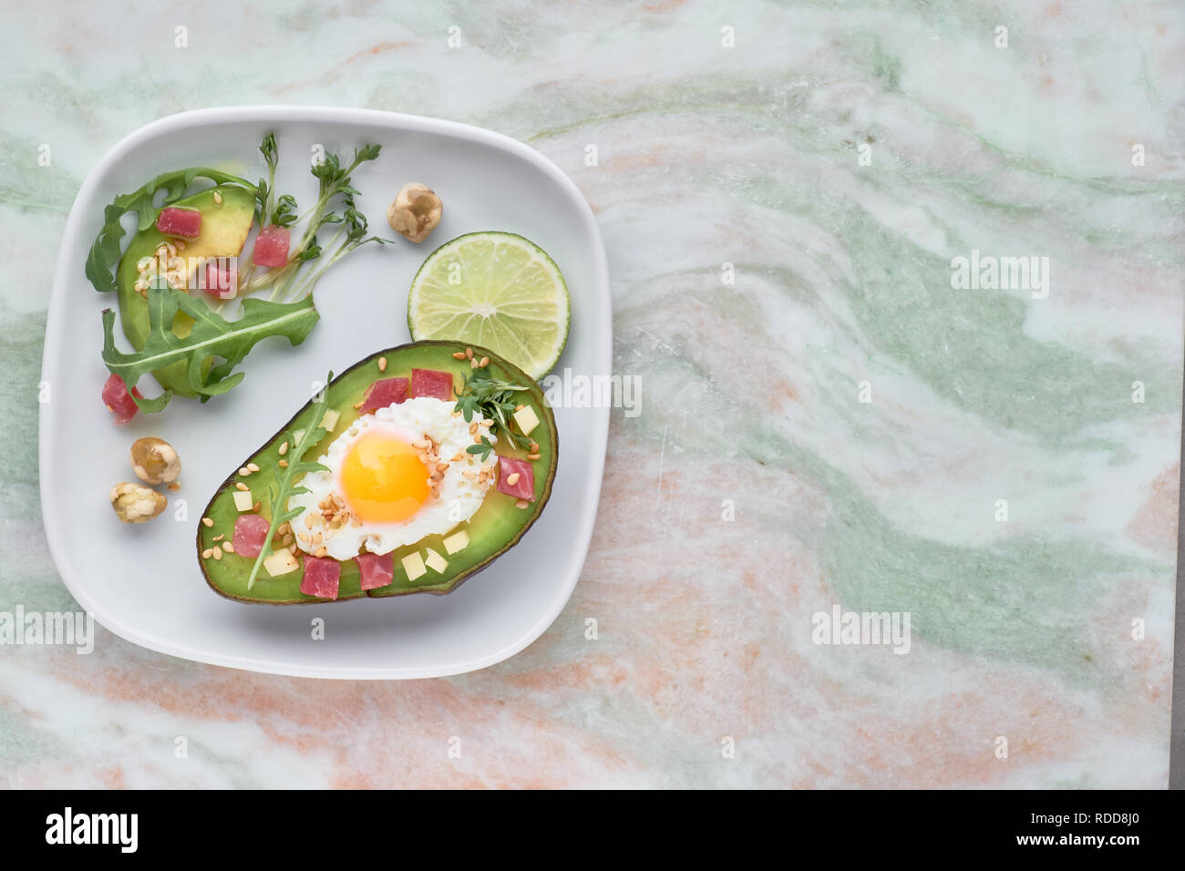 Keto Diät Teller: gebackene Avocado Boot mit Schinken würfeln, Wachtel Ei und Käse mit grünen Rucola Salat serviert. Stockfoto