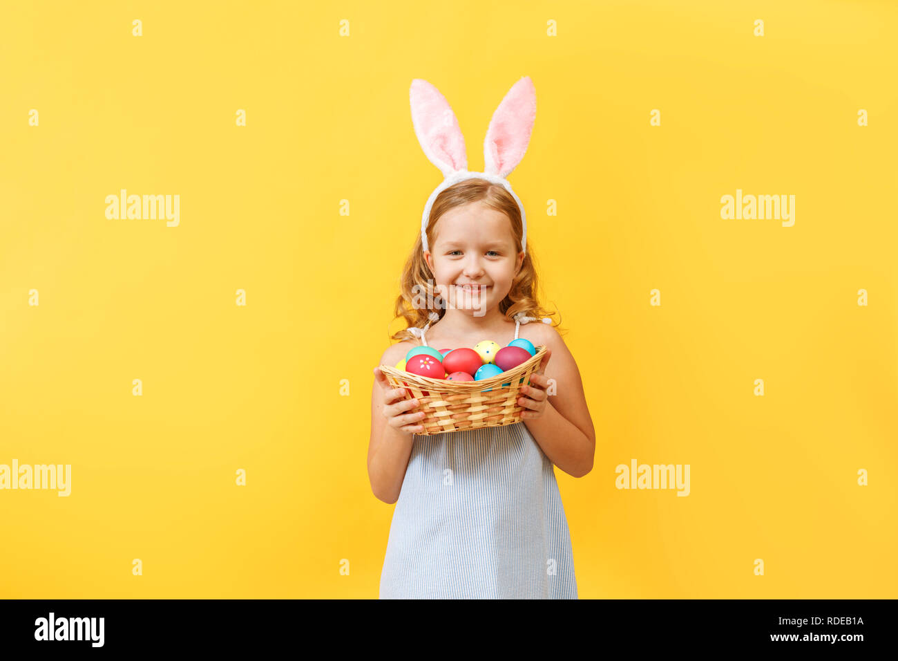 Süßes kleines Kind Mädchen mit Hasenohren holding Warenkorb der Ostereier auf einem farbigen Hintergrund. Stockfoto