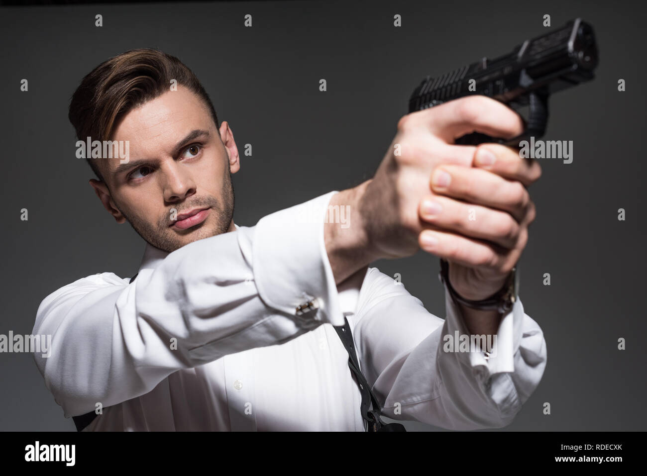 Stattliche Secret Agent mit Pistole isoliert auf Grau Stockfoto