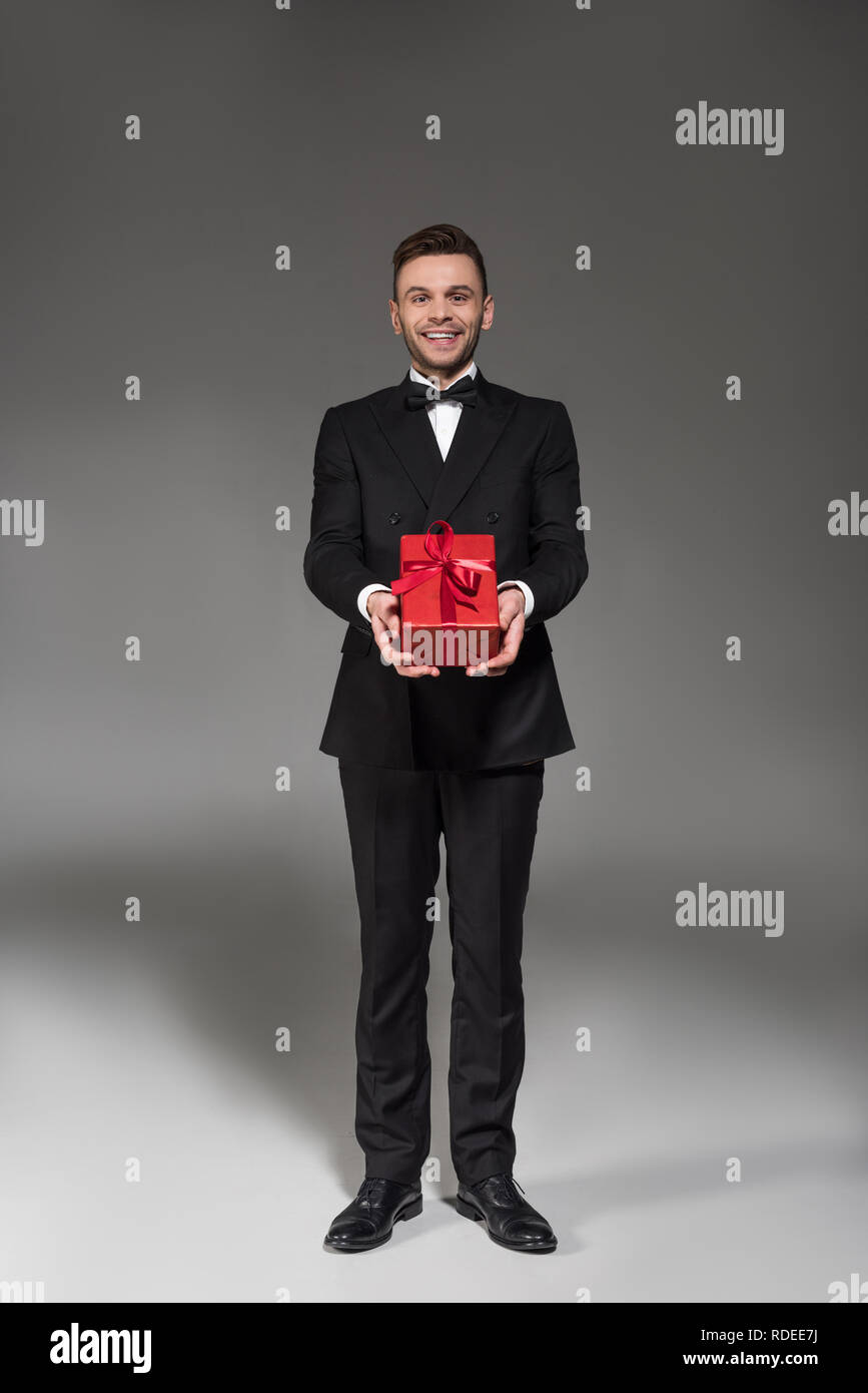 Schöne elegante Mann im schwarzen Smoking und Fliege gifting Rot auf Grau Stockfoto