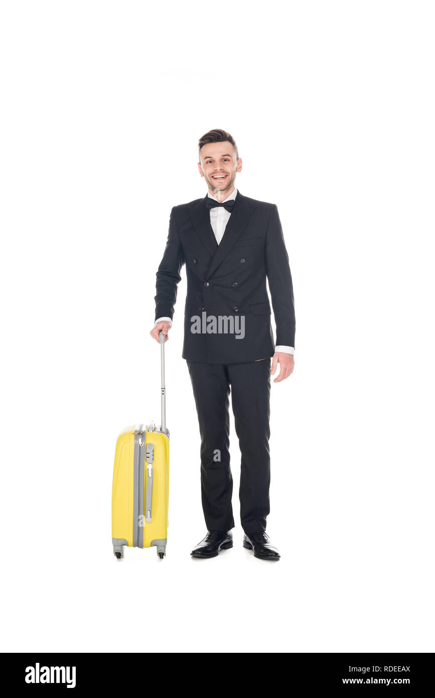 Lächelnd elegante Mann im schwarzen Smoking mit Travel Bag isoliert auf weißem Posing Stockfoto