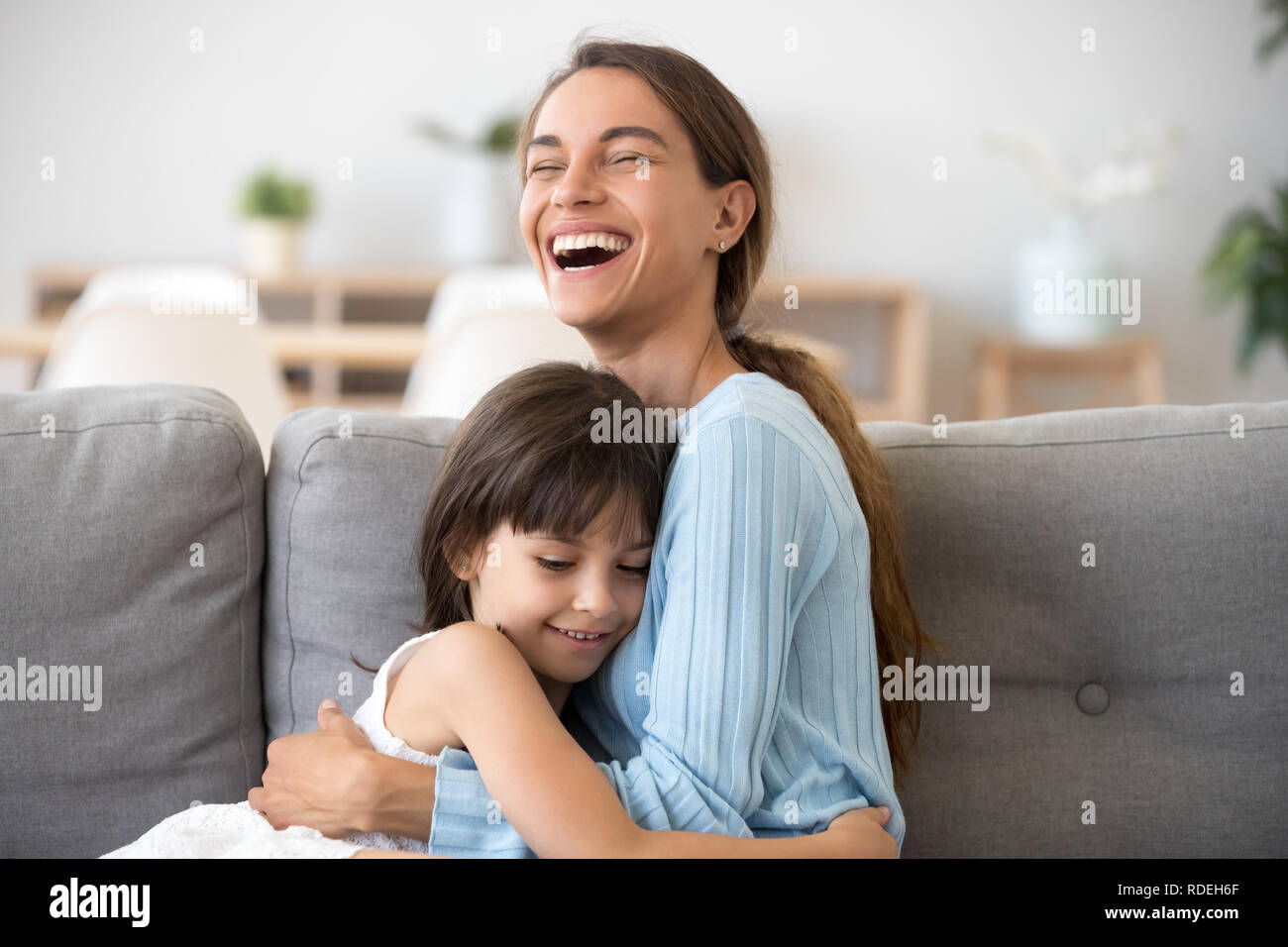 Fröhliche Mutter lachend umarmt cute kid Tochter auf Sof sitzen Stockfoto