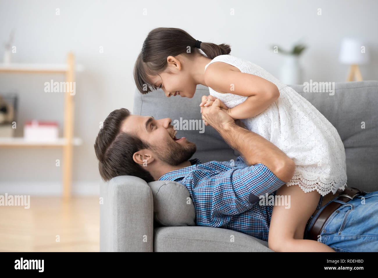 Gerne Vater und Kind Mädchen halten sich an den Händen spielen auf Sofa Stockfoto