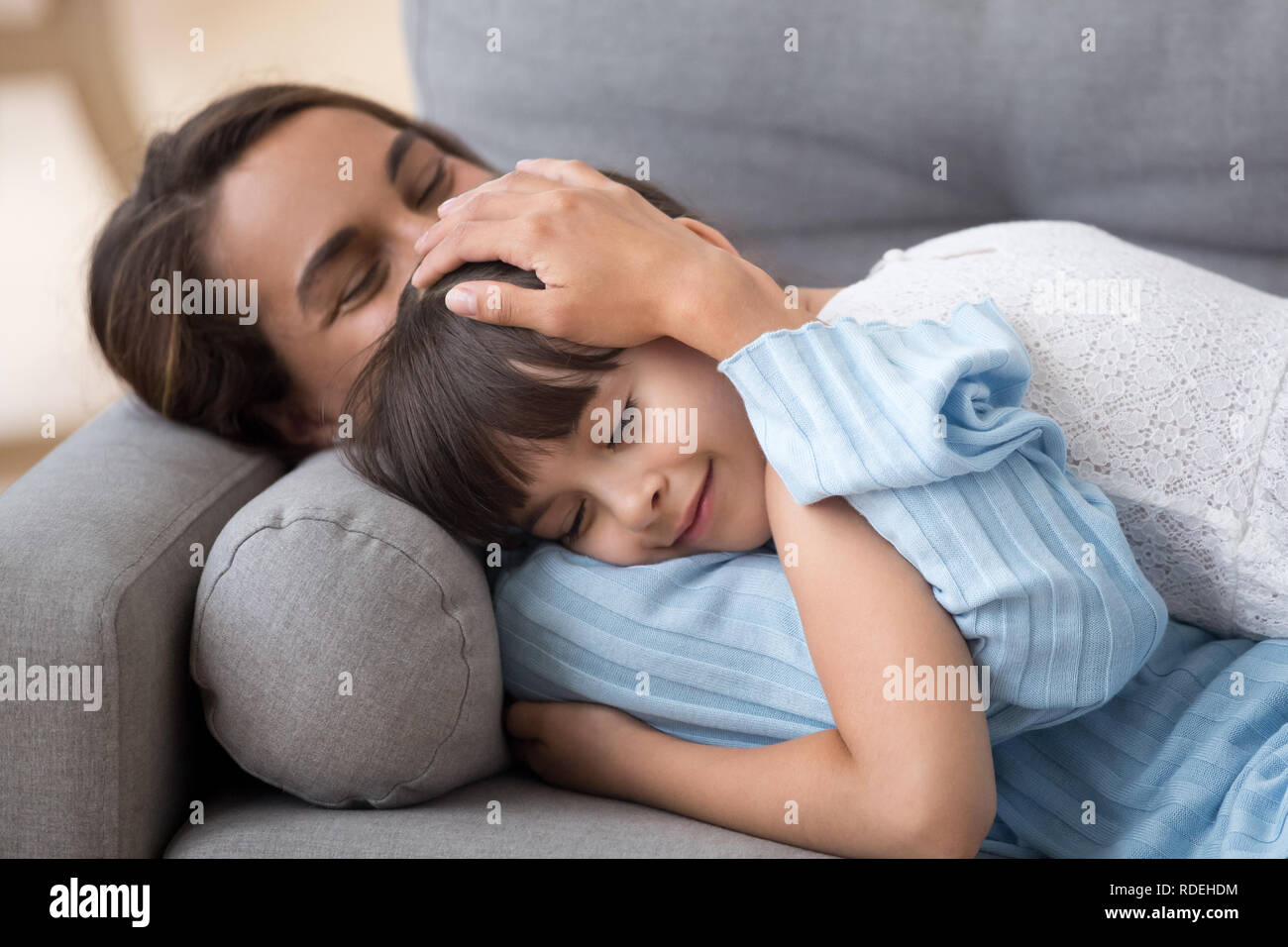 Liebevolle Mutter liebkosen süsse kleine Tochter liegend auf dem Sofa toget Stockfoto