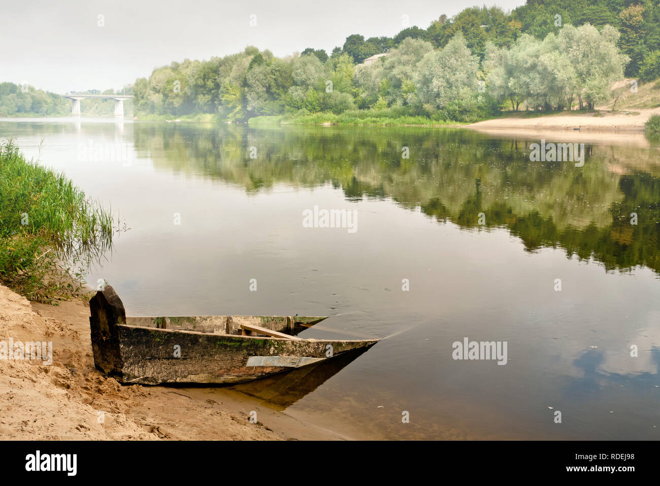 Ein altes Holzboot Hälfte untergetaucht im Wasser auf einem nebligen Sommer Morgen mit Blick auf die Brücke Stockfoto